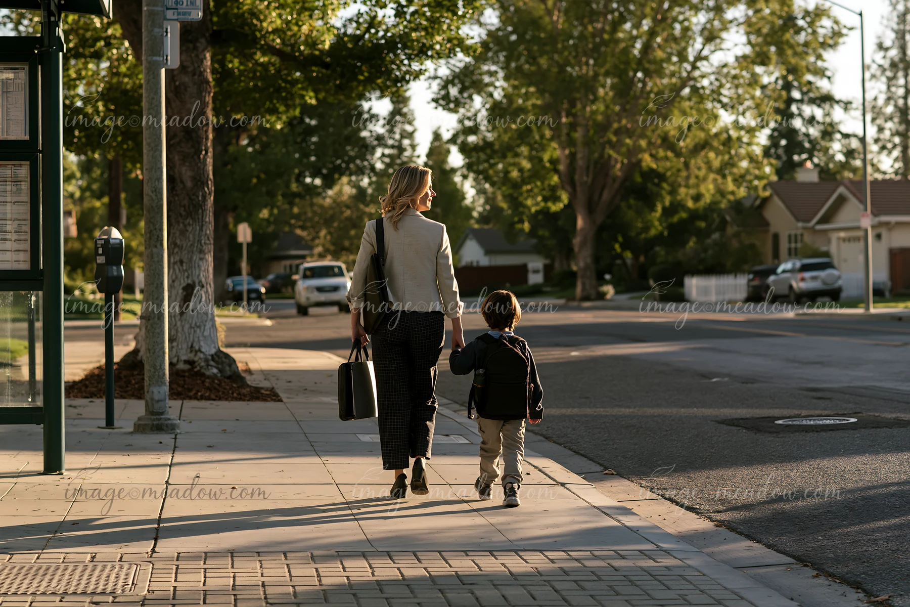 A businesswoman walks hand-in-hand with a child along a sidewalk near homes.