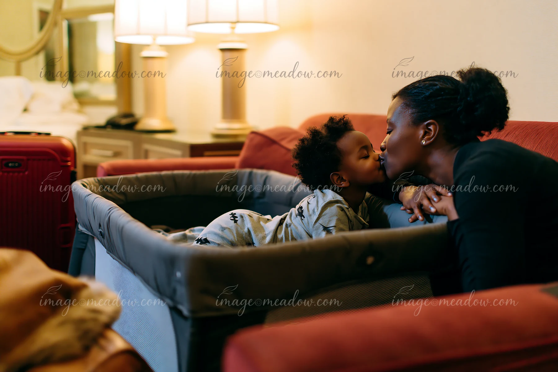 A child kisses a parent at bedtime in a cozy hotel room, showing their bond.