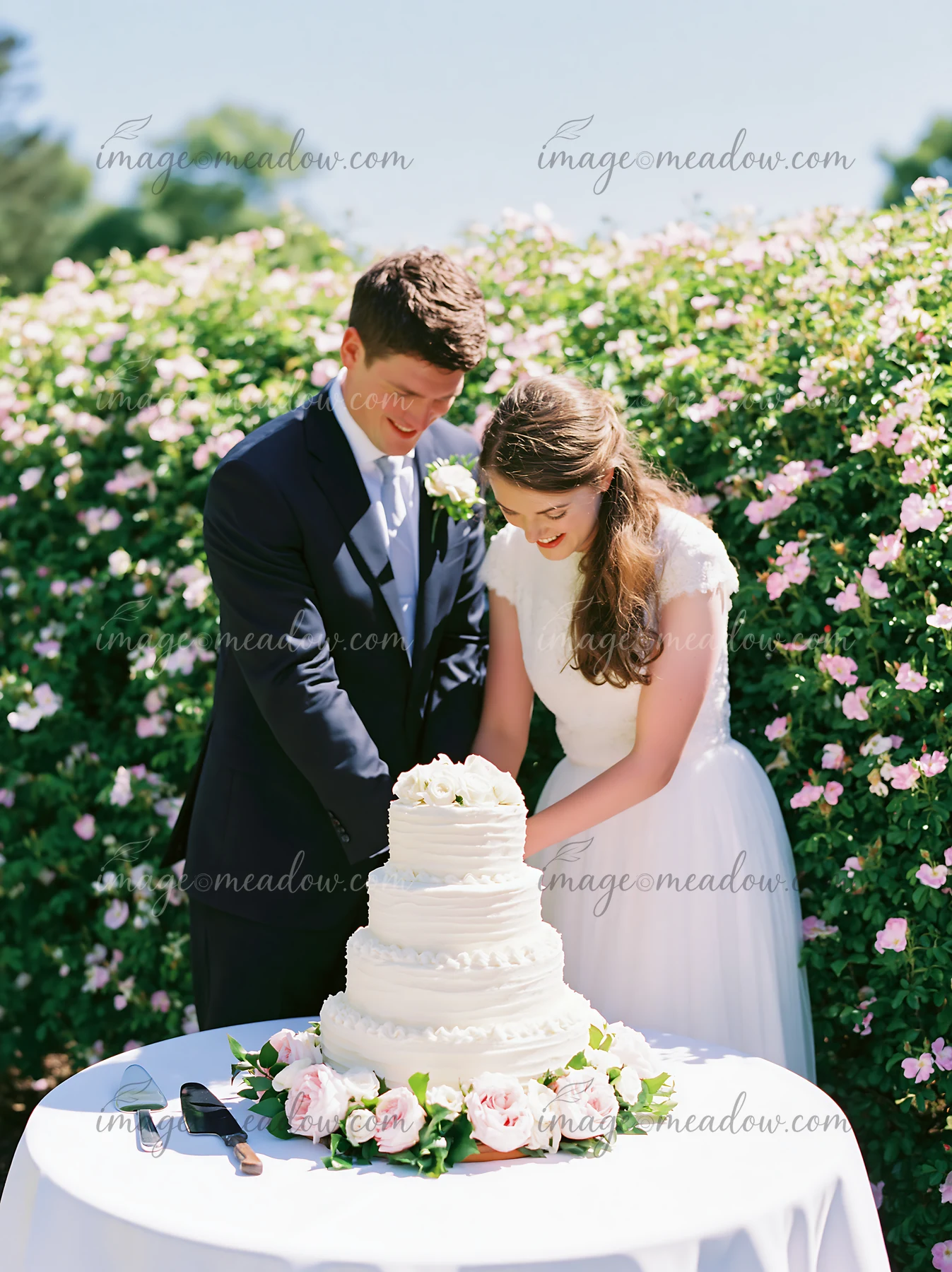 A couple is cutting a wedding cake surrounded by flowers at a garden reception.
