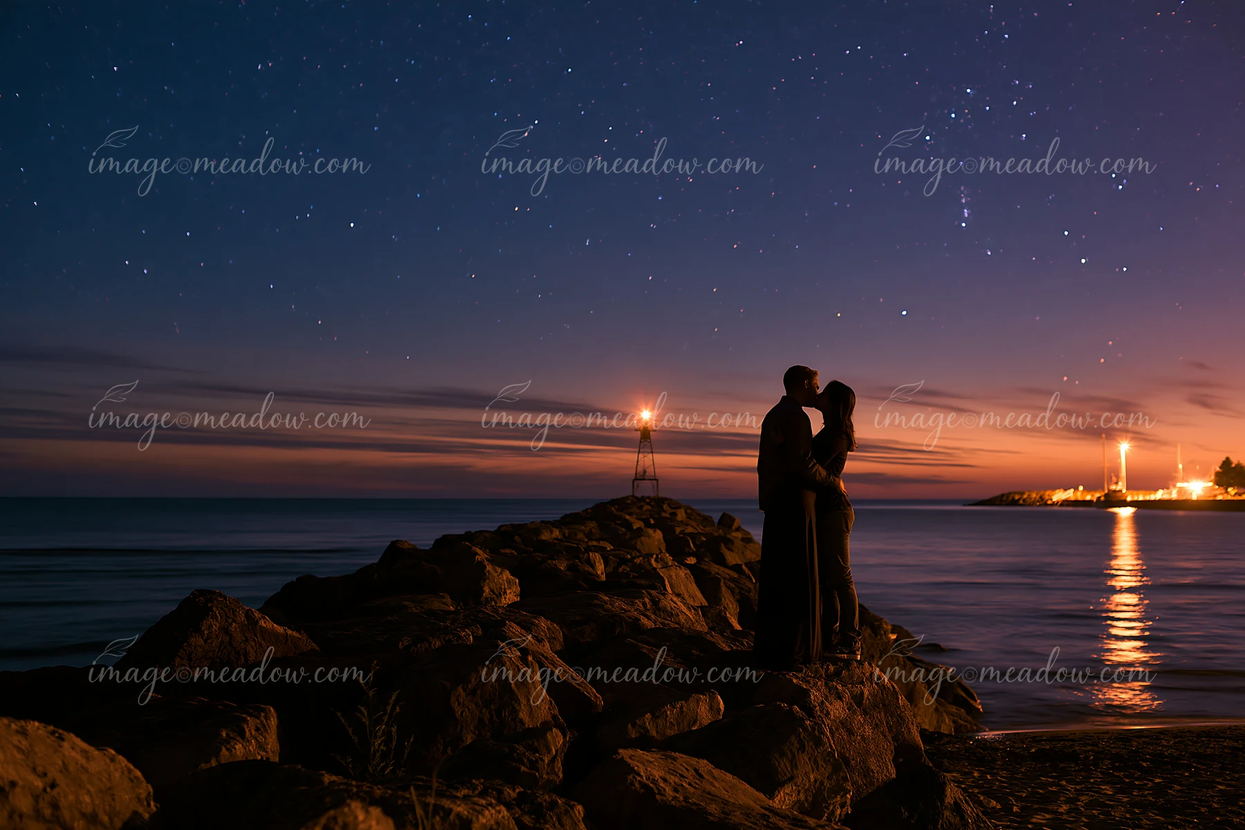 A couple shares a kiss silhouetted against a starry sky at the beach.