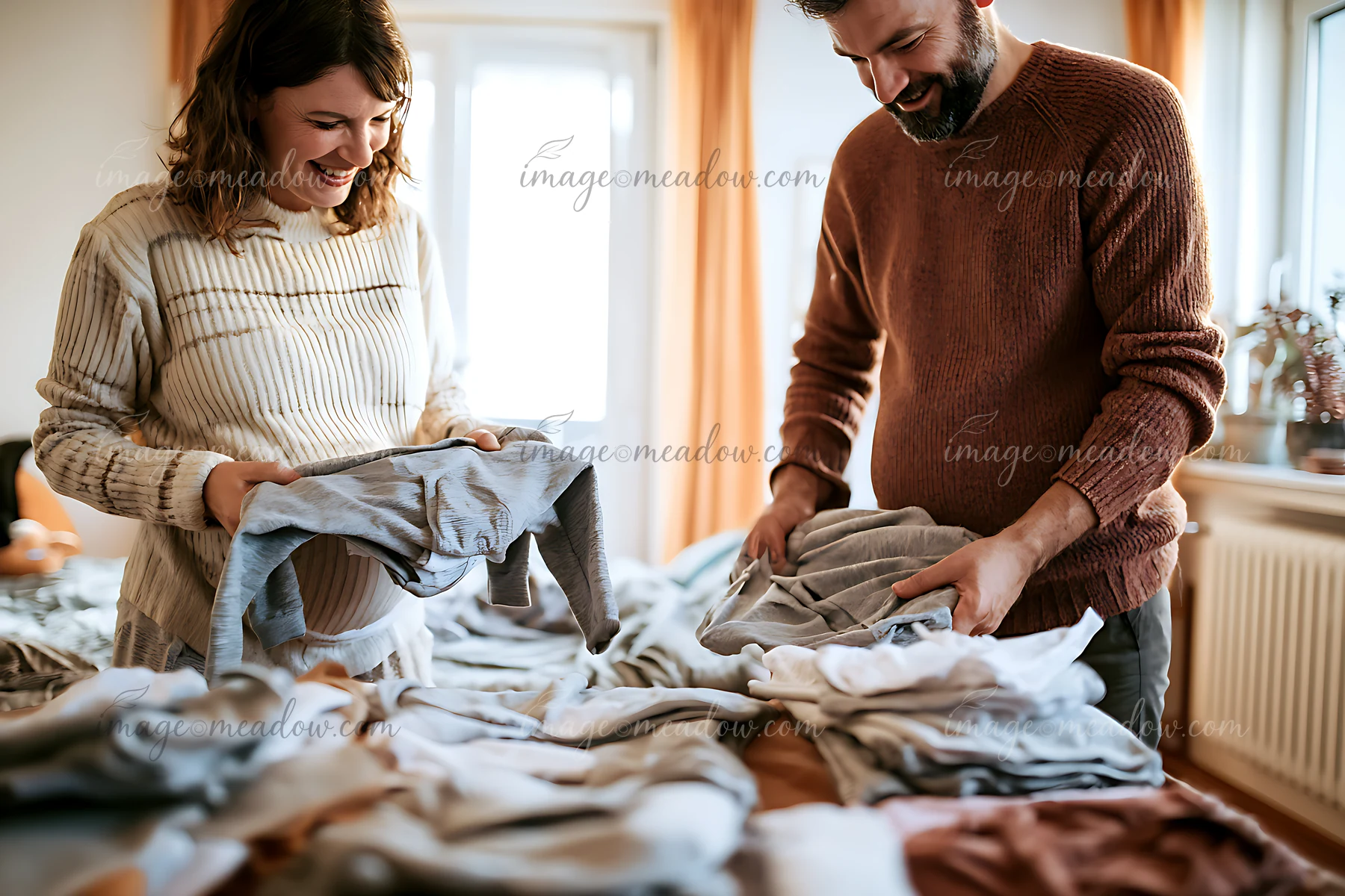 A couple sorts and organizes baby clothes in their cozy living room, celebrating their upcoming arrival.