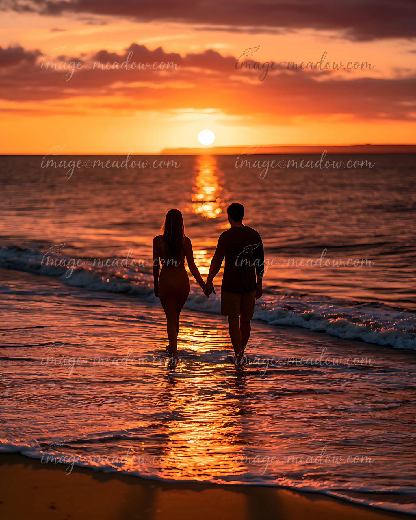 A couple walks hand in hand along the shoreline as the sun sets over the ocean.