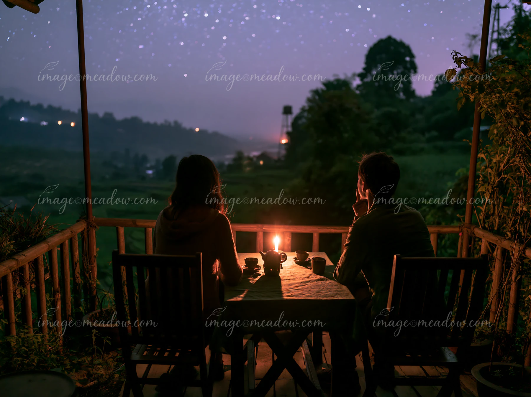 A couple watching stars from a balcony sits at a table with a candle.