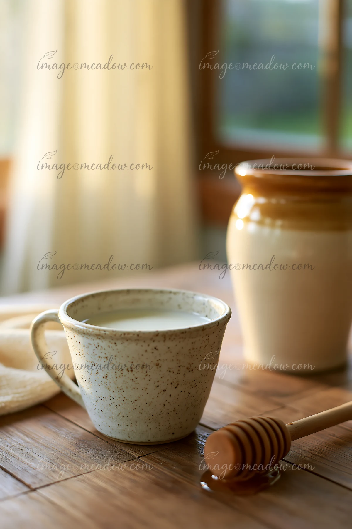 A cup of cream is placed next to a honey dipper on a wooden table, with a pottery jar in the background.