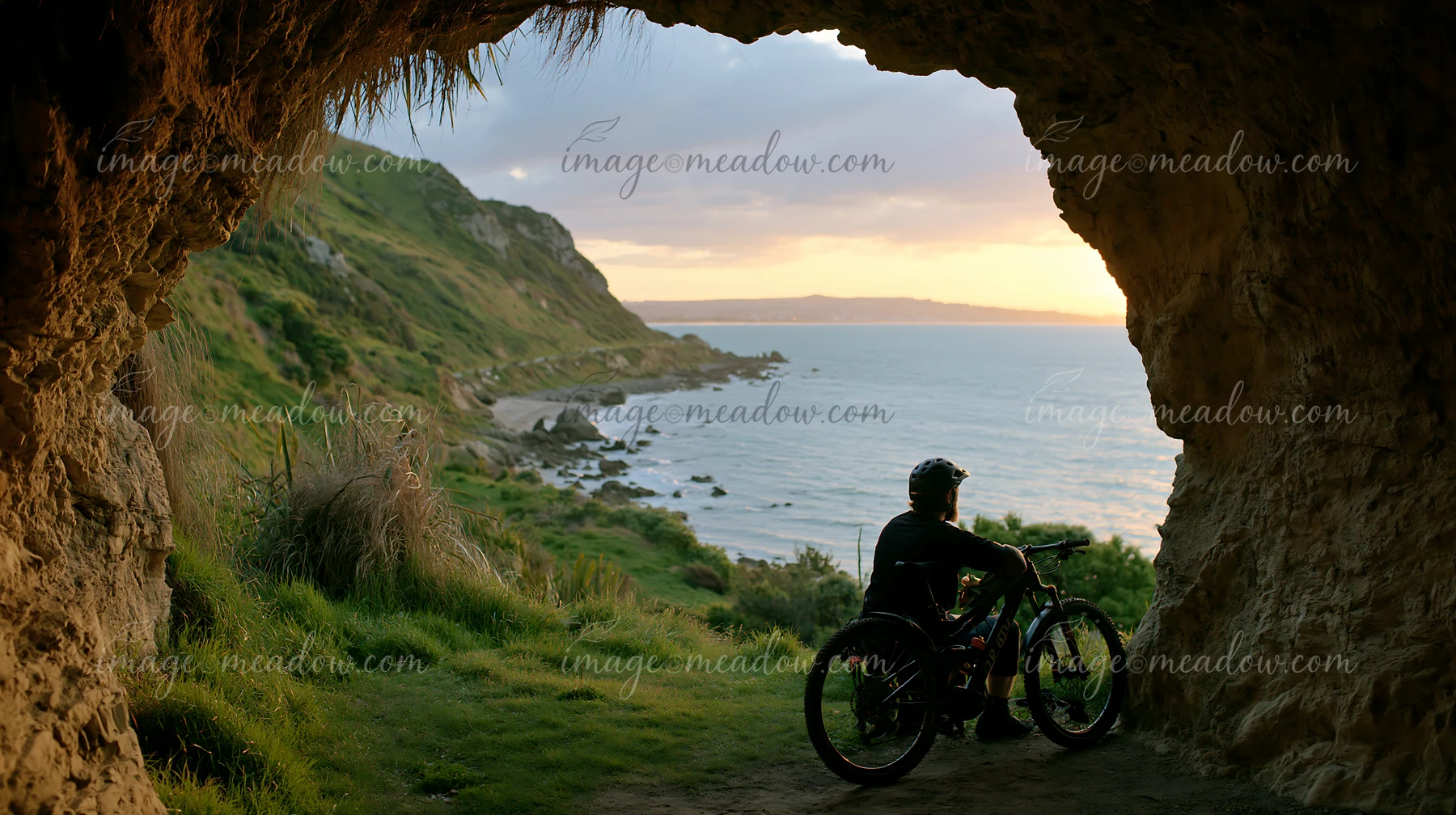 A cyclist sits on a bike while looking out at the coastline viewed through sea cave.
