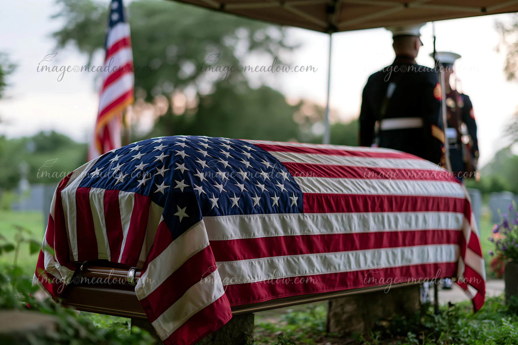 A flag-draped coffin during veteran funeral service is presented under a tent in a cemetery.