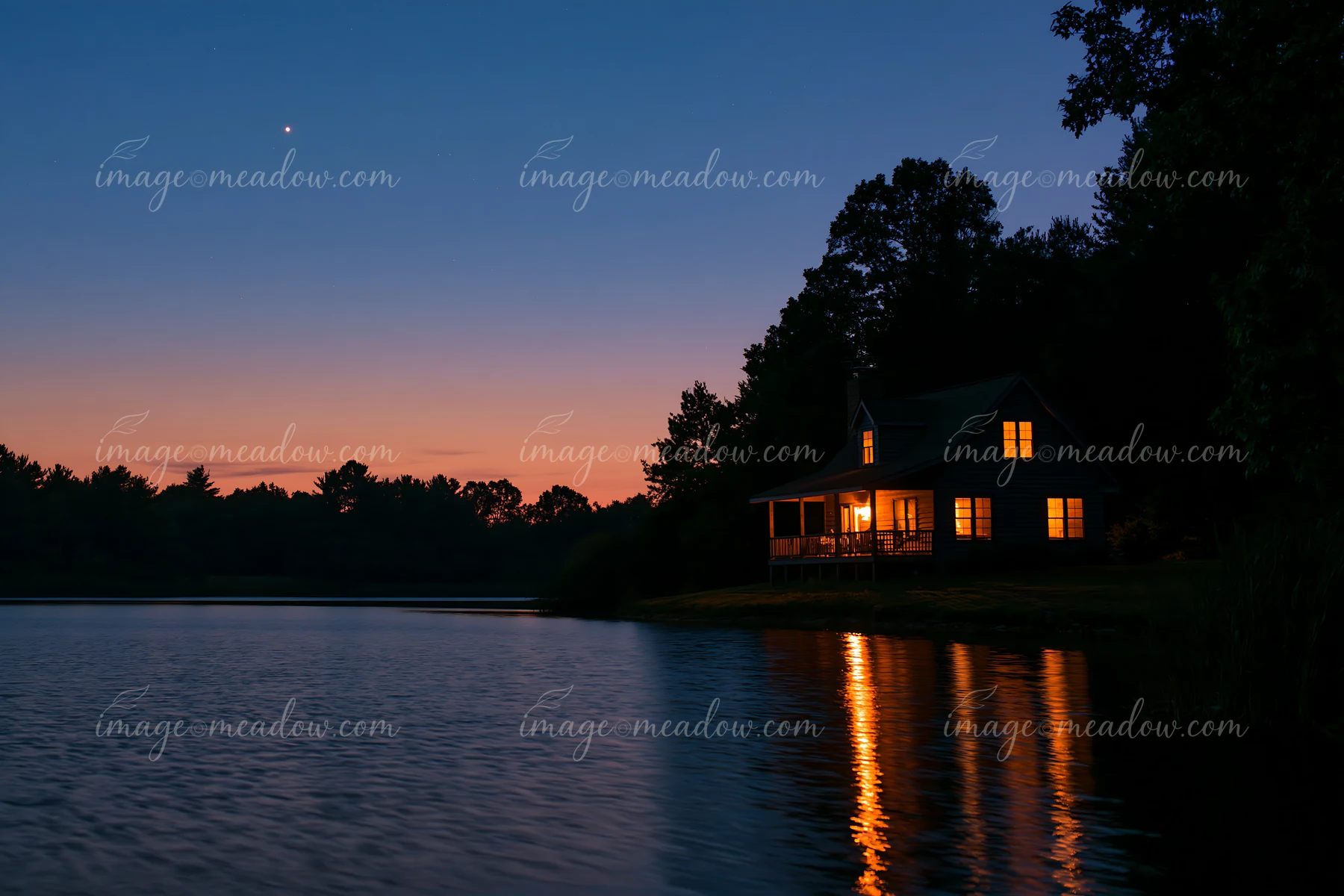 A holiday home under stars stands near a lake as the sun sets, reflecting warm light on the water.