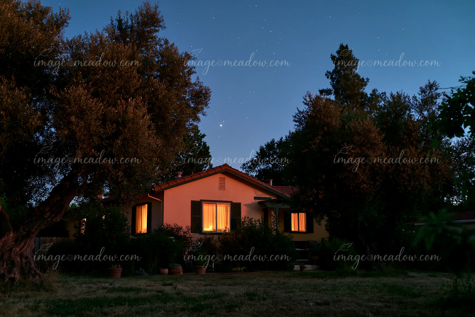 A house under stars during blue hour is visible with warm light shining from the windows.
