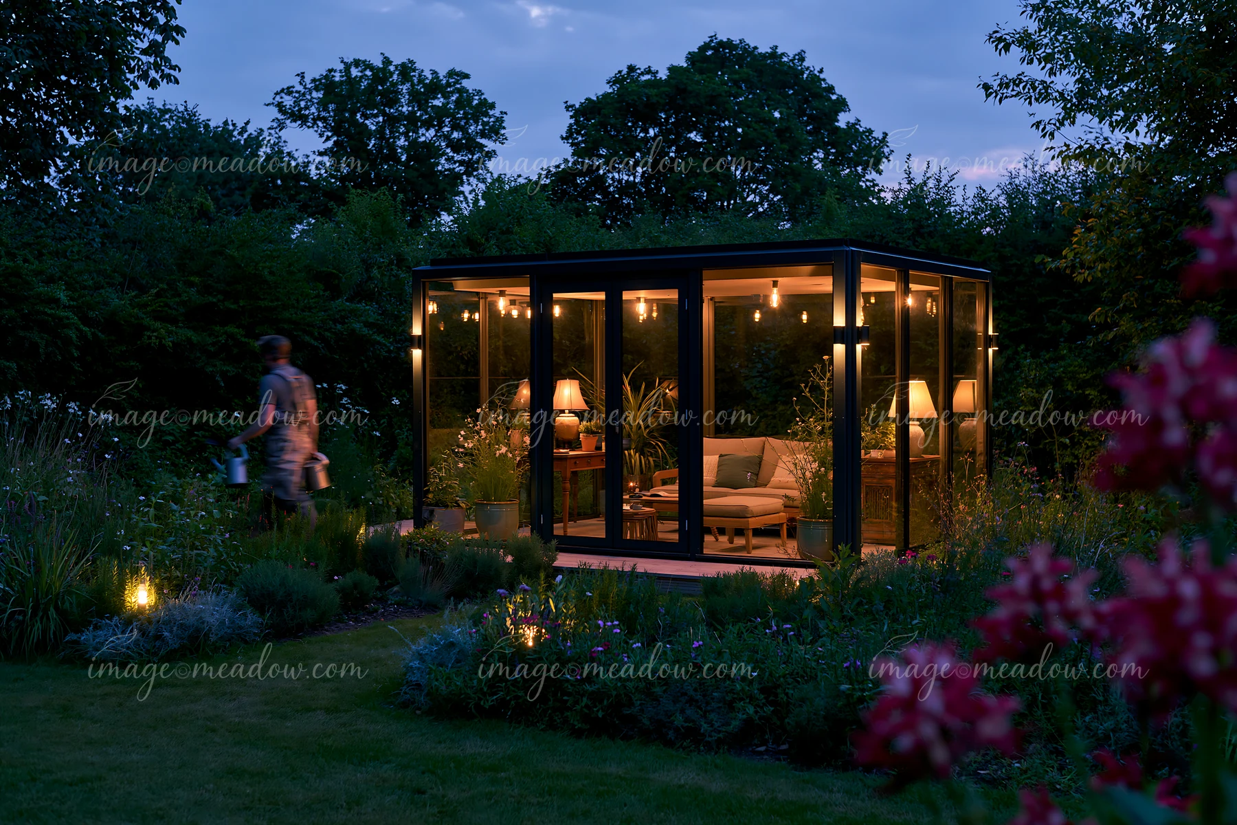 A modern glass garden pavilion with night lighting stands in a garden.