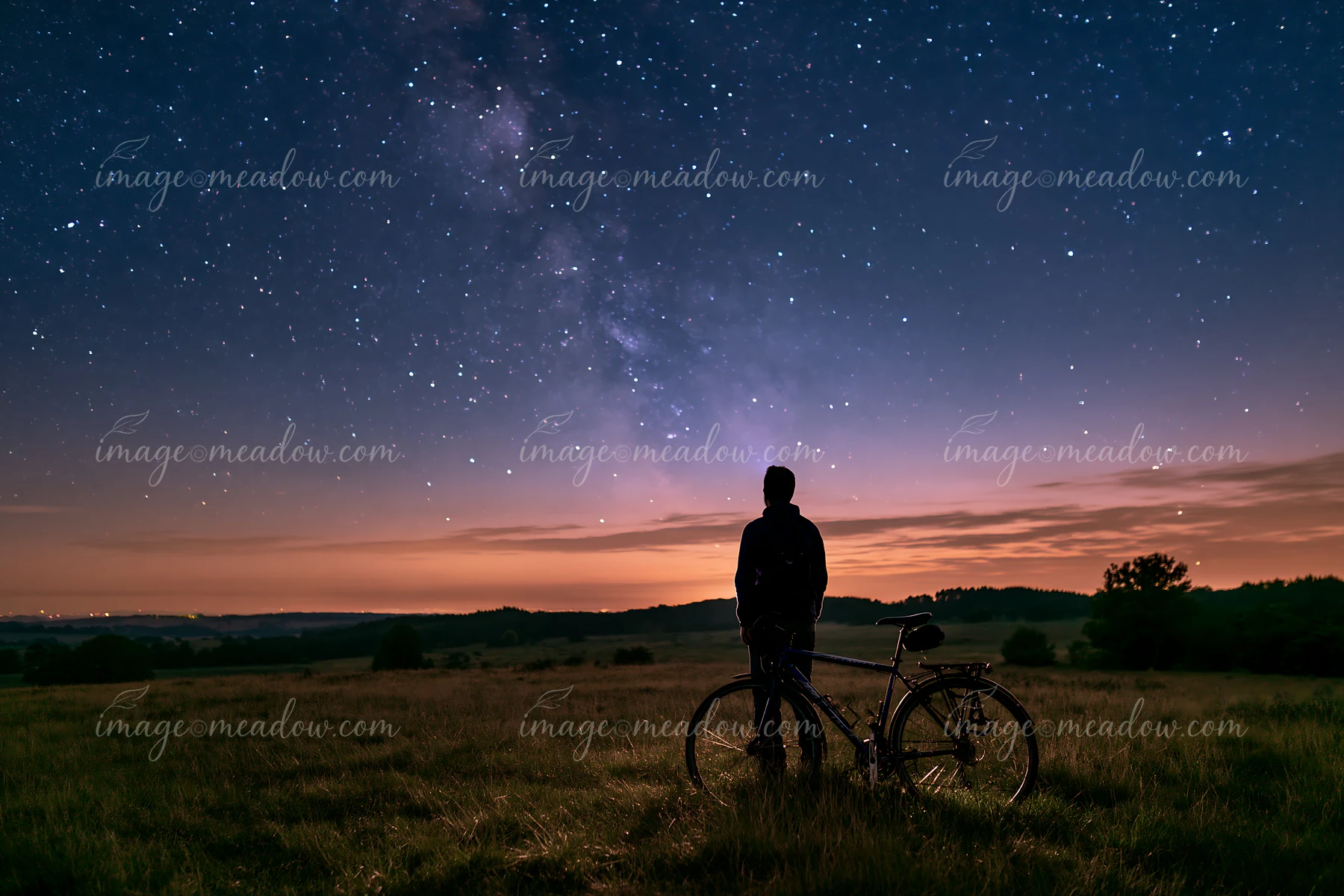 A person stands beside a bicycle, gazing up at a starry sky.