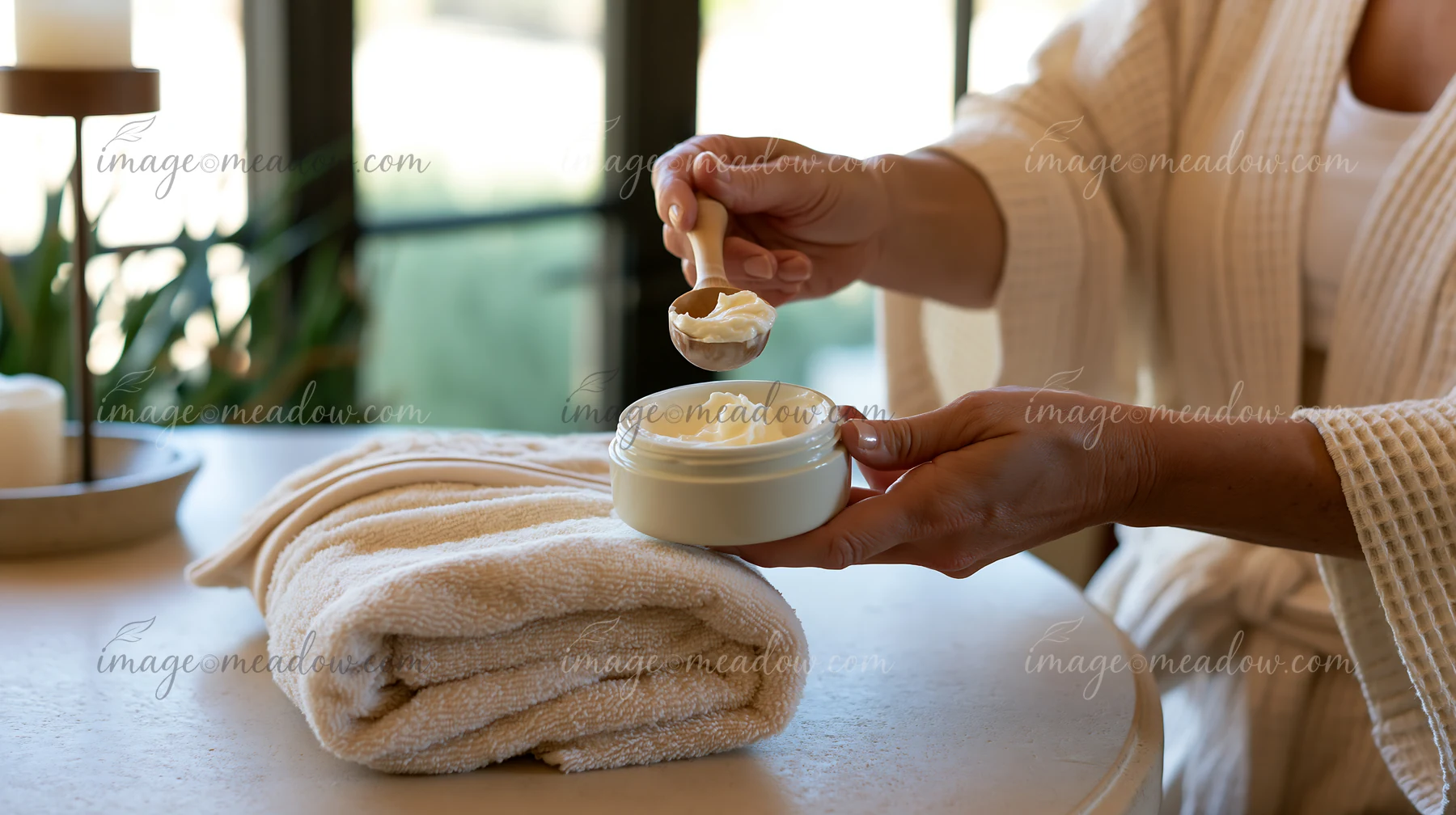 A person uses a scoop to measure a cream dose from a jar while resting on a towel.