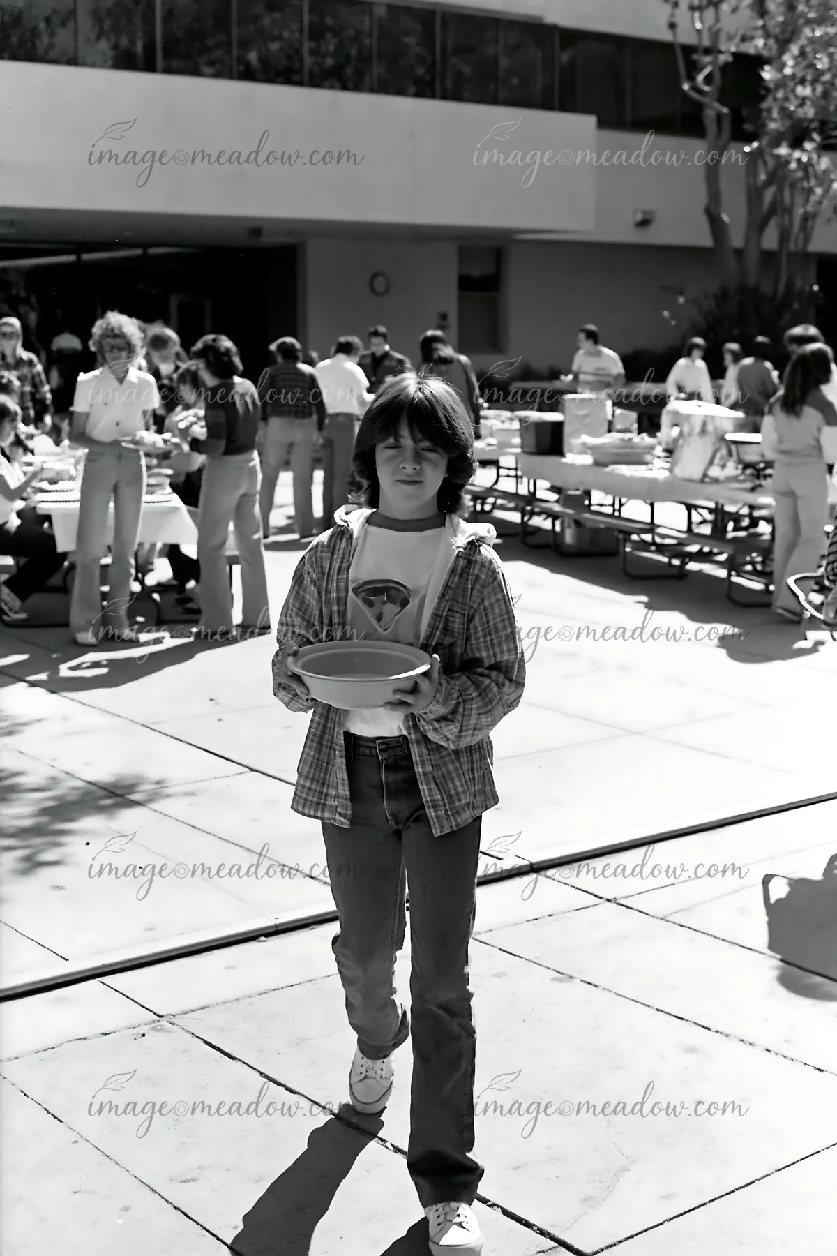 A person walks across an outdoor area holding a bowl at a community potluck buffet.