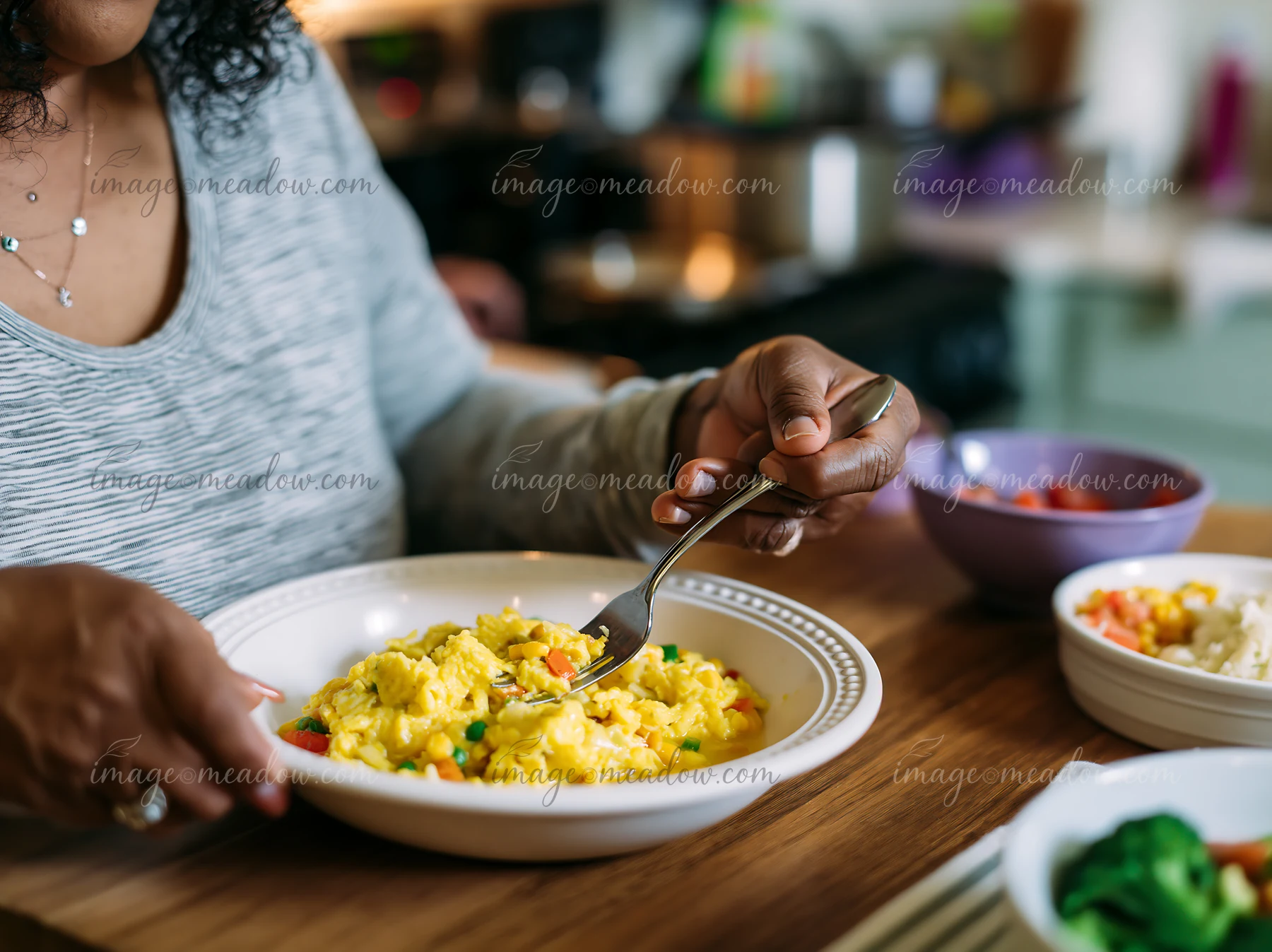 A person with limited hand mobility using utensils to eat scrambled eggs in a home kitchen.