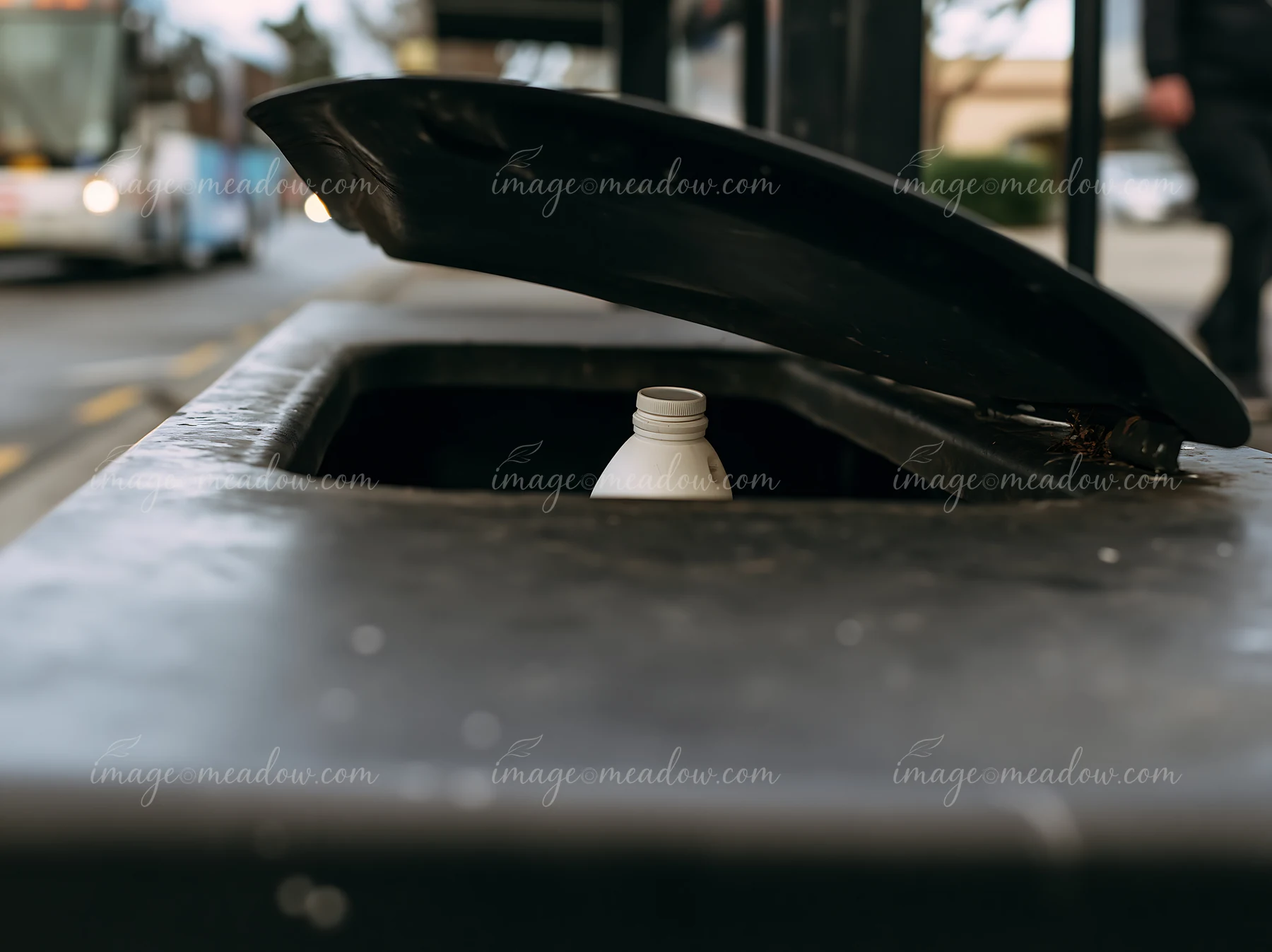 A recycling bin is open, showing a milk bottle placed inside on a busy urban street.