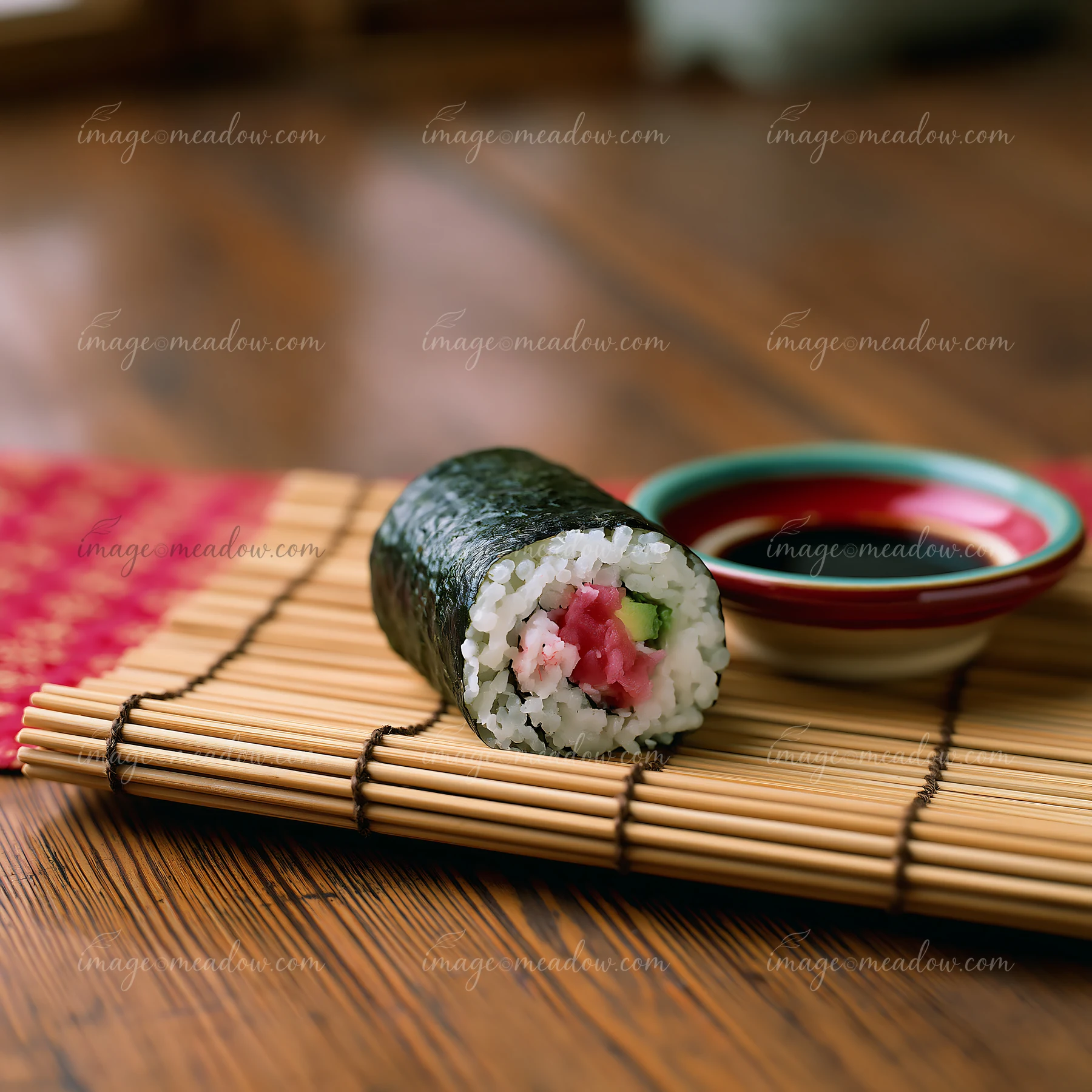 A single sushi roll on bamboo mat sits next to a small dish of soy sauce.