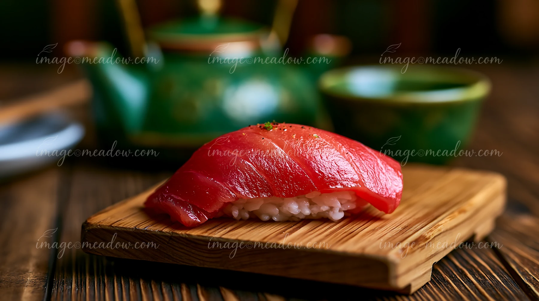 A single tuna nigiri on wooden board sits beside a green tea set.