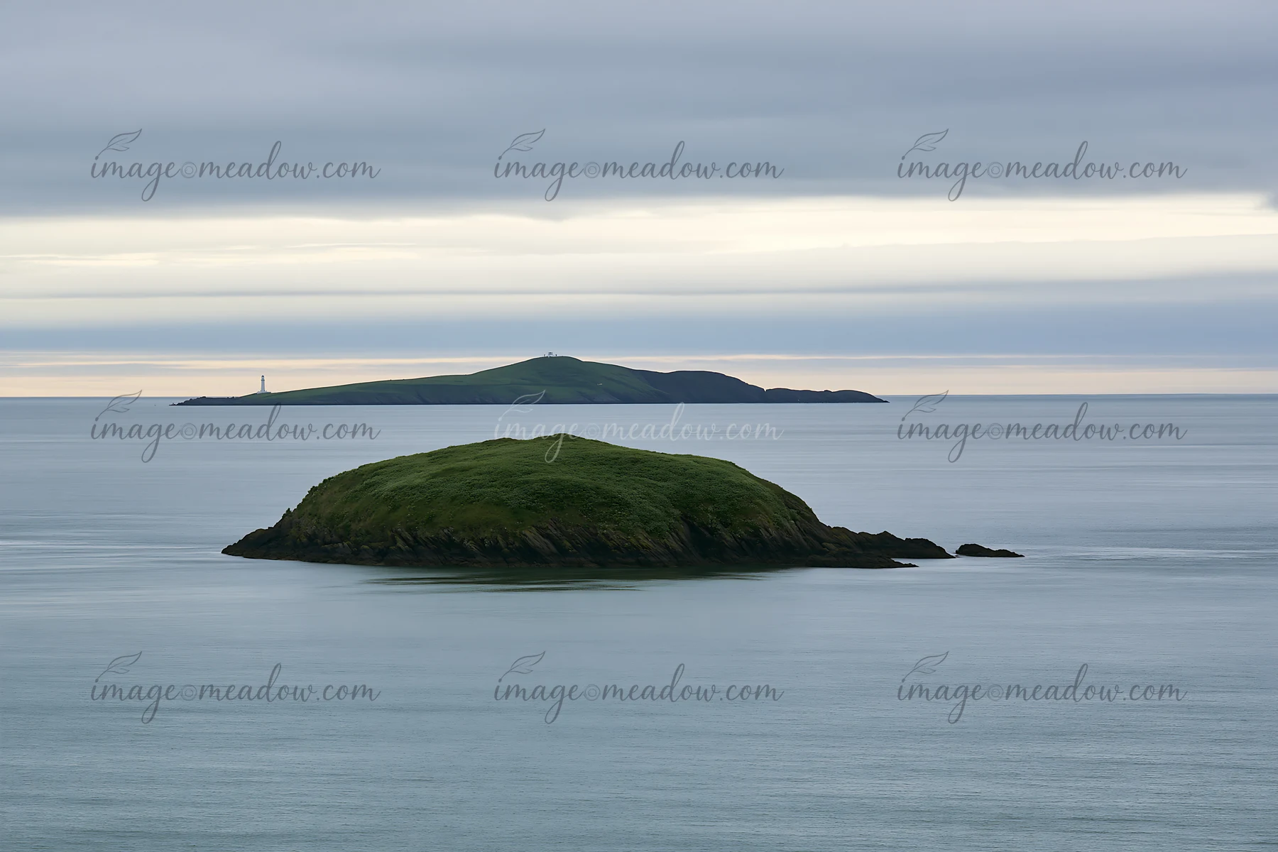 A small island with green vegetation is surrounded by water in a calm bay during sunset.
