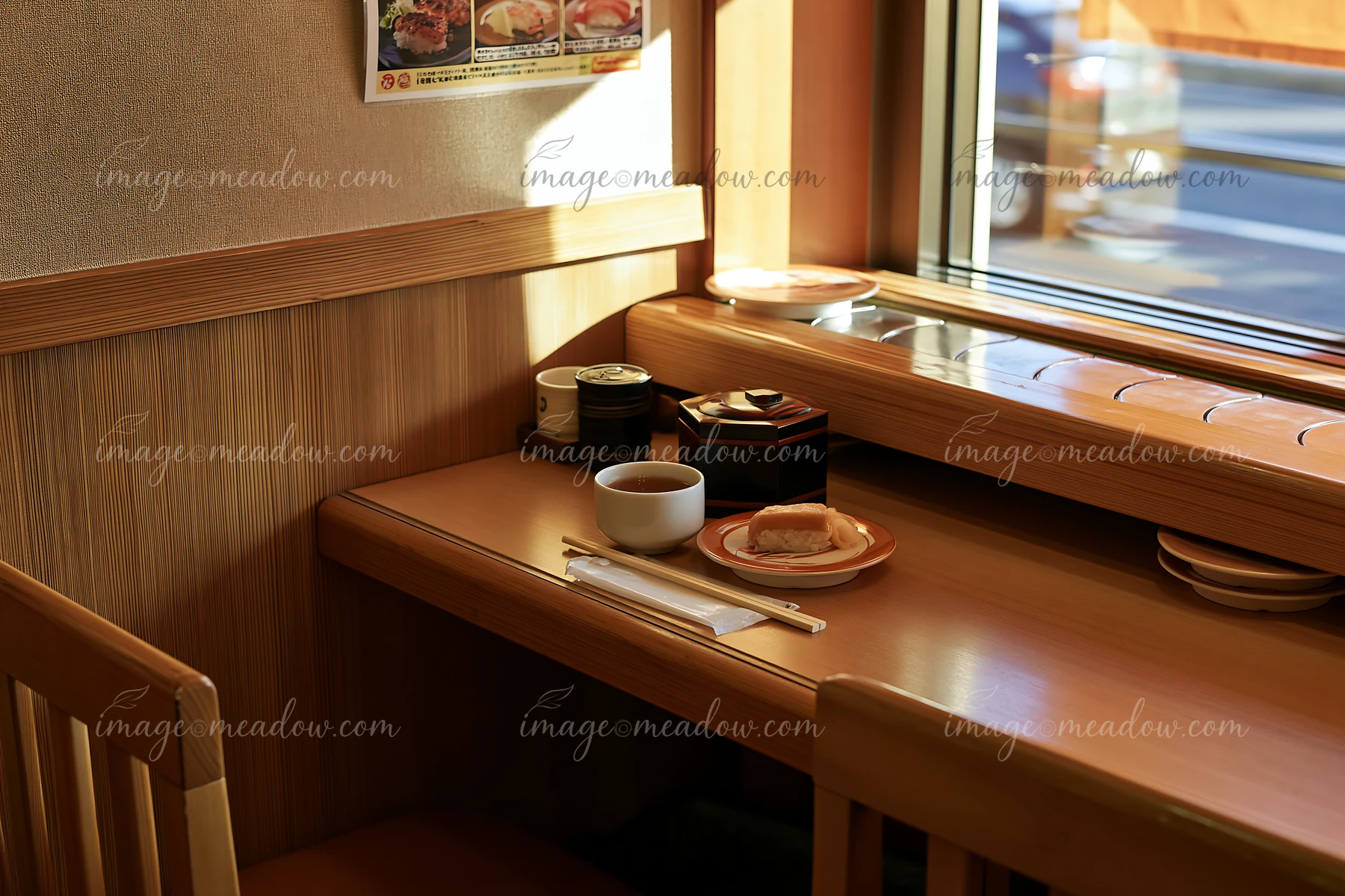 A small table in a sushi conveyor belt restaurant features a plate with sushi, a cup, and condiments.
