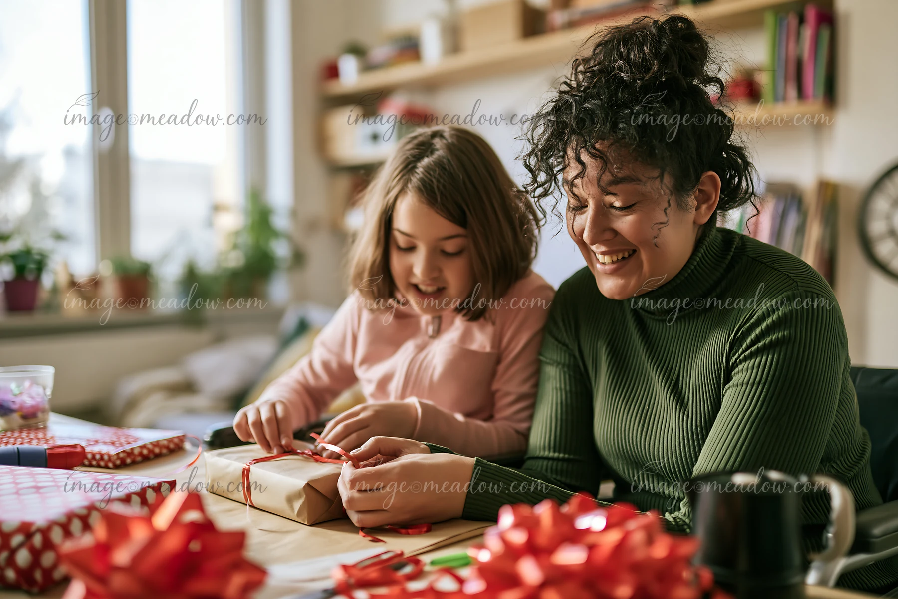 A smiling parent helps a child wrap a gift with paper and ribbon at a home table.