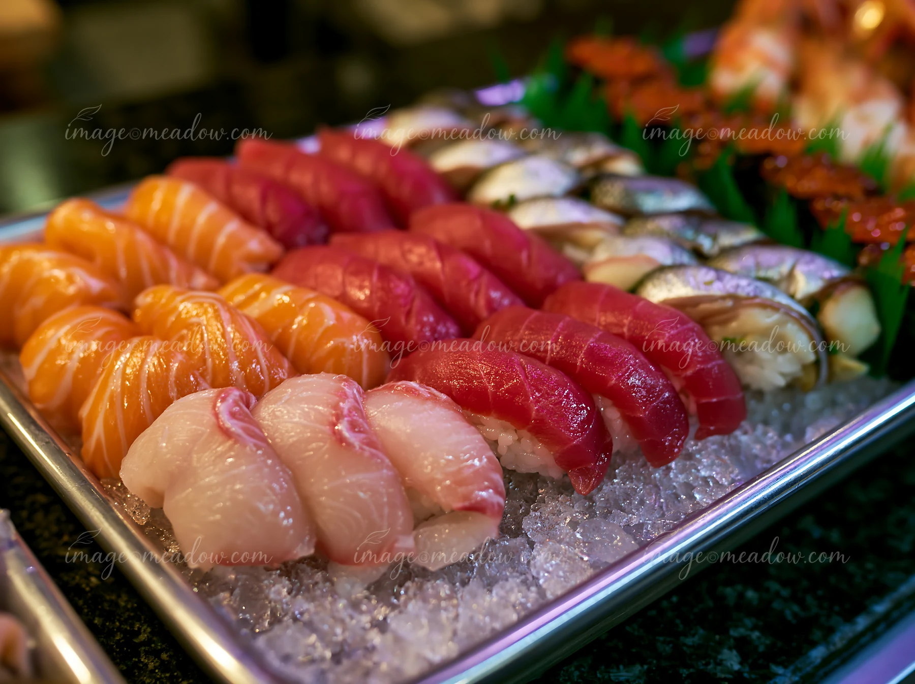 A variety of sushi types are arranged neatly on a tray filled with ice, showcasing vibrant colors and fresh seafood.