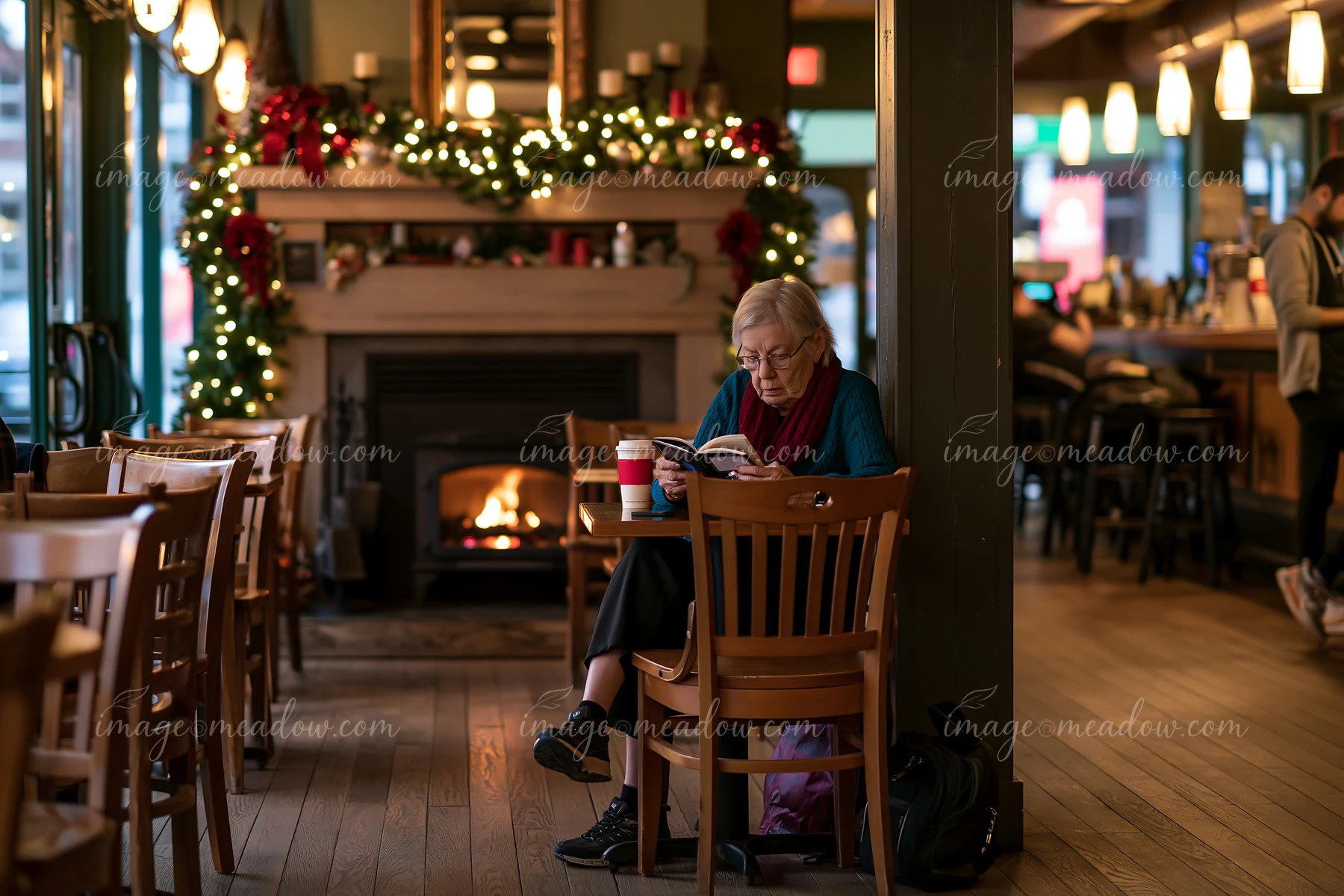 A woman sits in a festive coffee shop, reading while enjoying a drink.