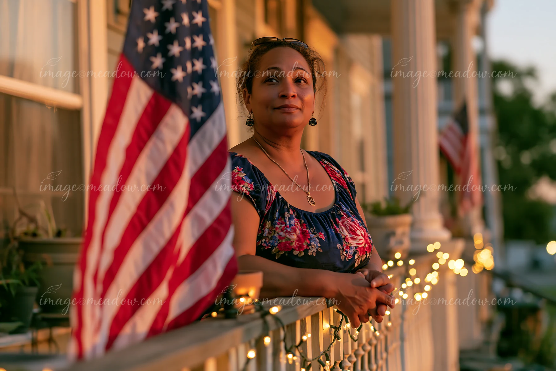 A woman stands on the balcony of an apartment building with an American flag outside.