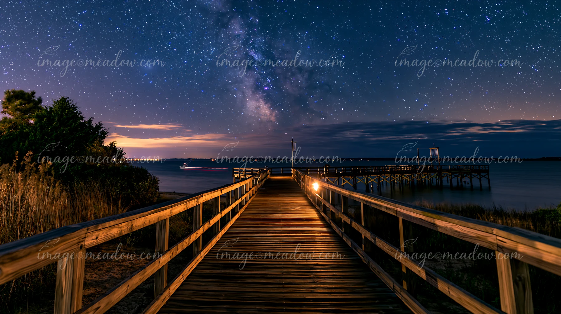 A wooden boardwalk extends into the water under a starry night over a coastal boardwalk.