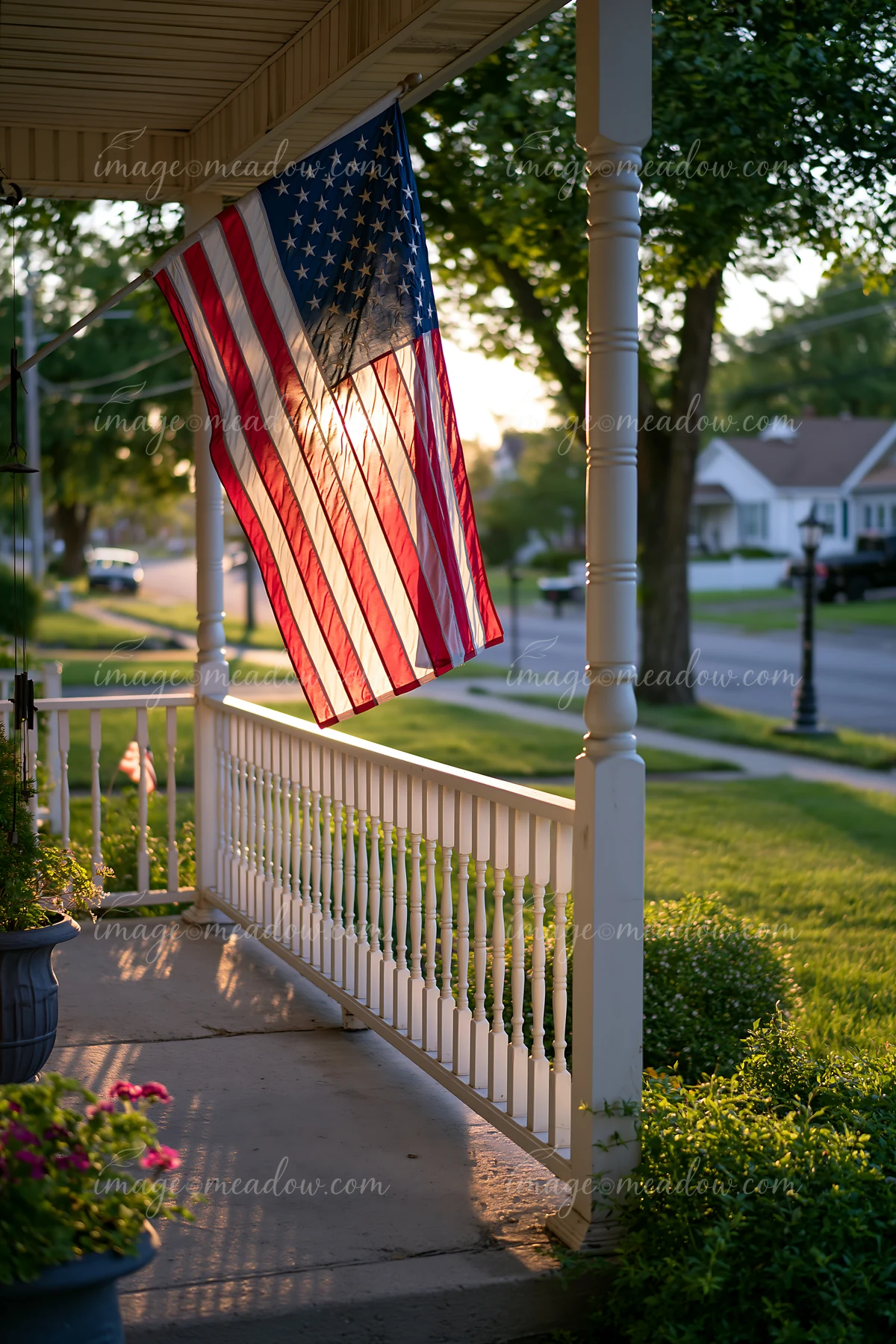 An American flag flying in strong wind is displayed on a porch during sunset.