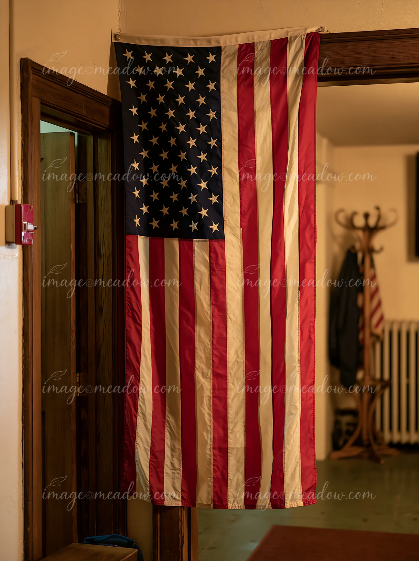 An American flag hanging vertically is displayed inside a room with wooden features.
