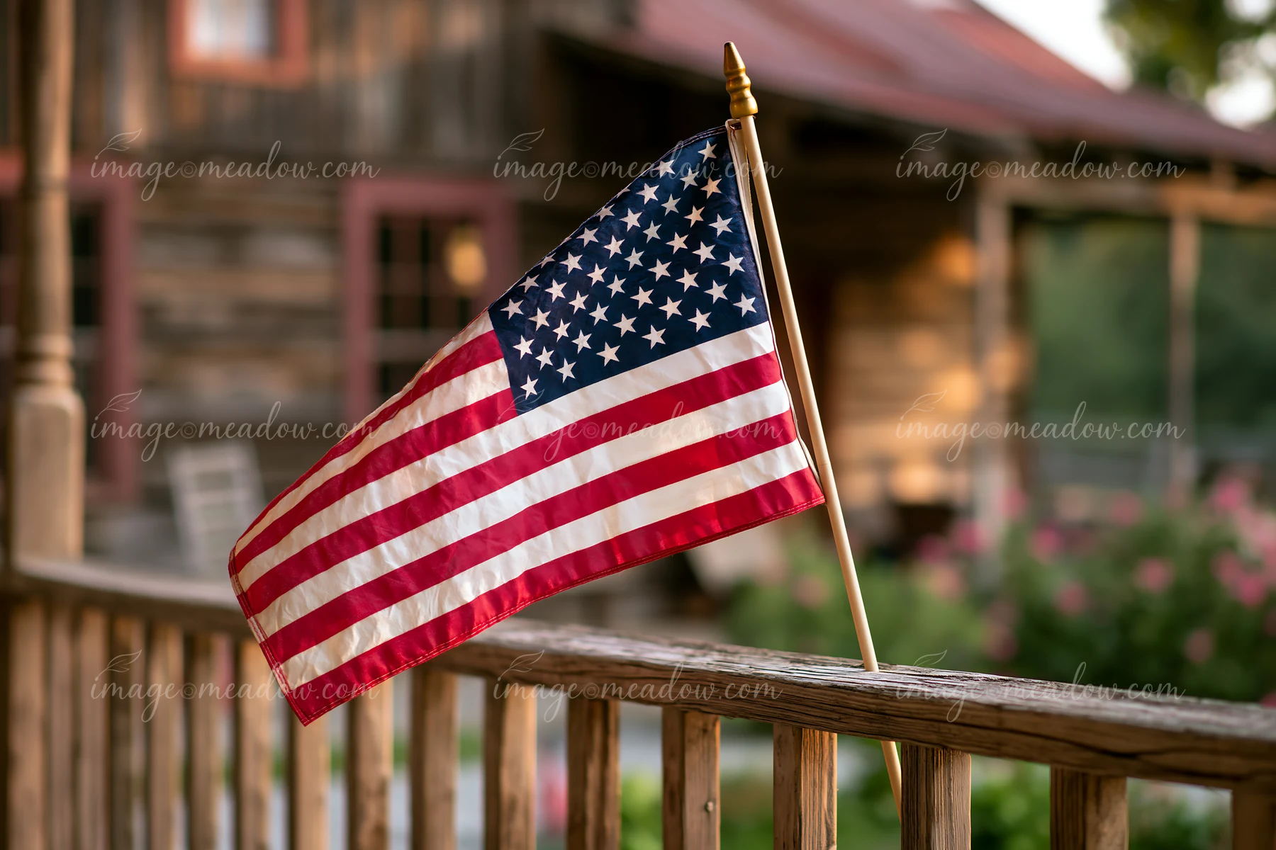 An American flag waving in gentle breeze is displayed on a wooden porch of a rustic cabin.