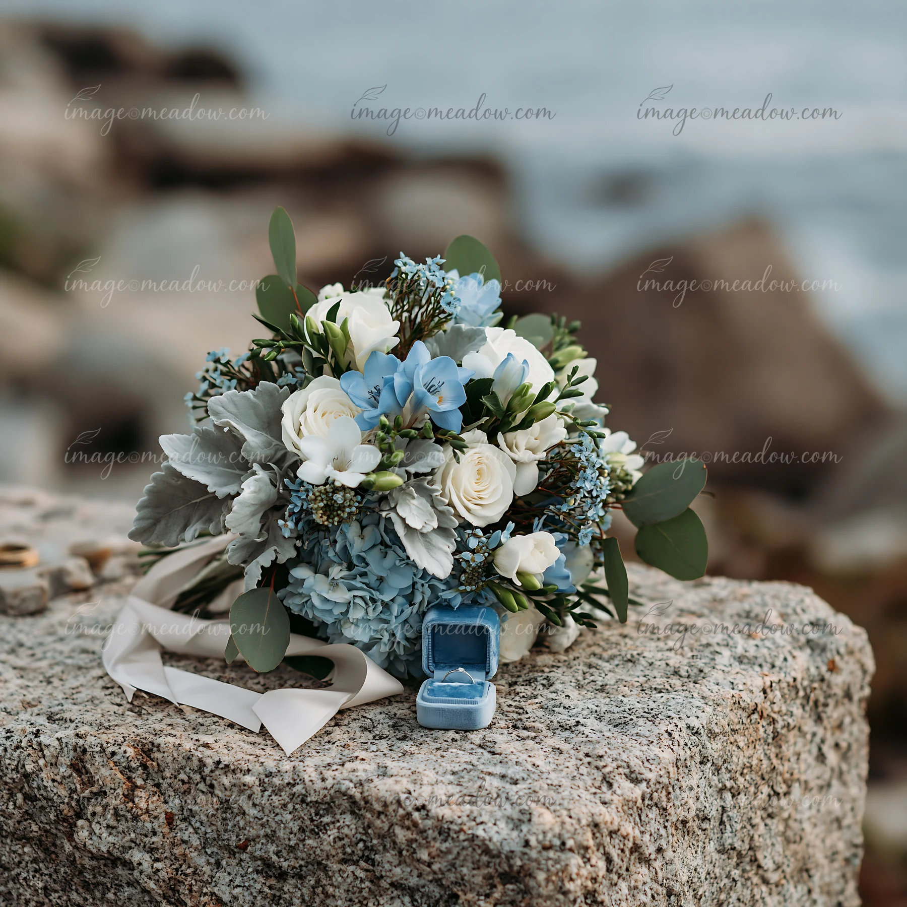 Blue and white wedding bouquet with an open ring box rests on a textured stone altar.