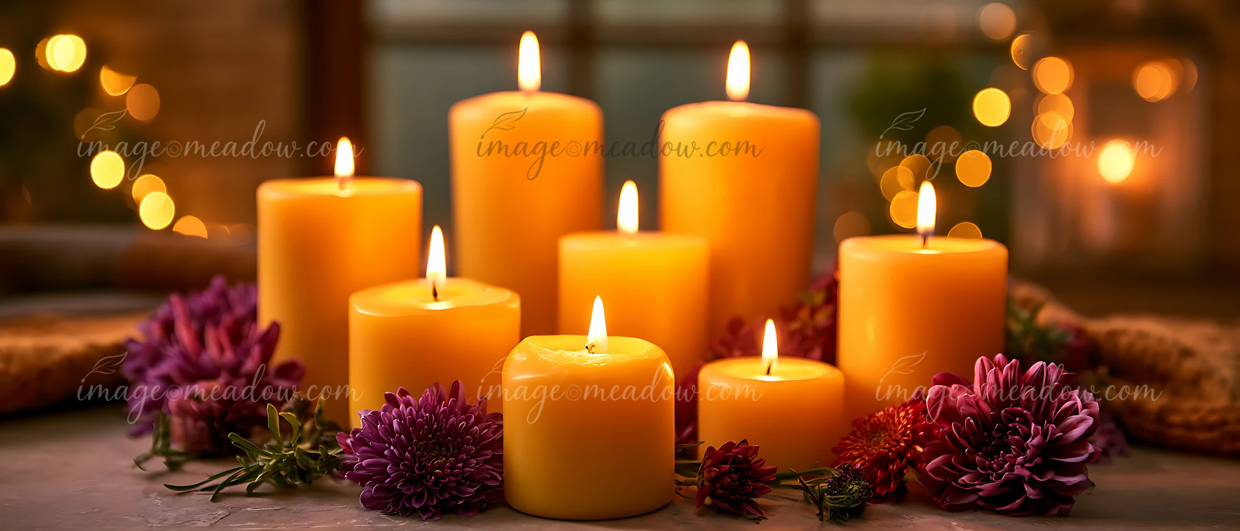 Candles are lit and arranged on a table with purple and yellow flowers around them.