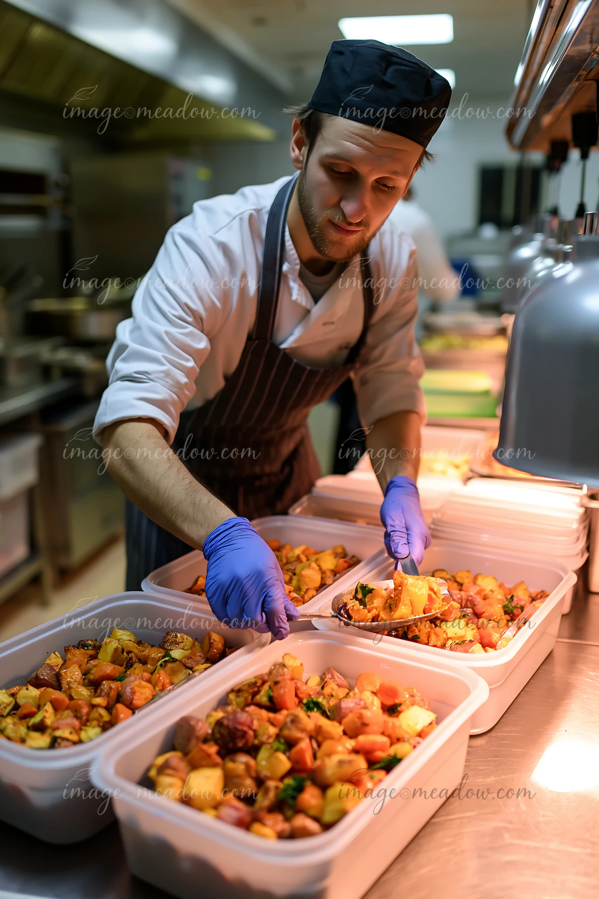 Chef in gloves serves roasted vegetables into containers during Christmas dinner preparation in a commercial kitchen.