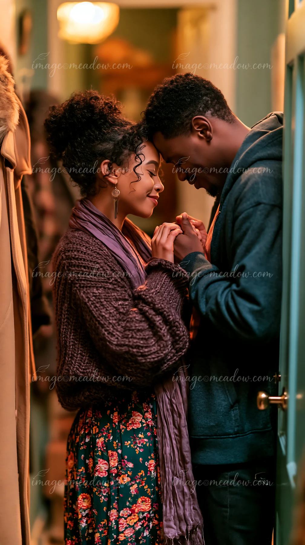 Couple shares a tender hand kiss in a warmly lit indoor doorway.