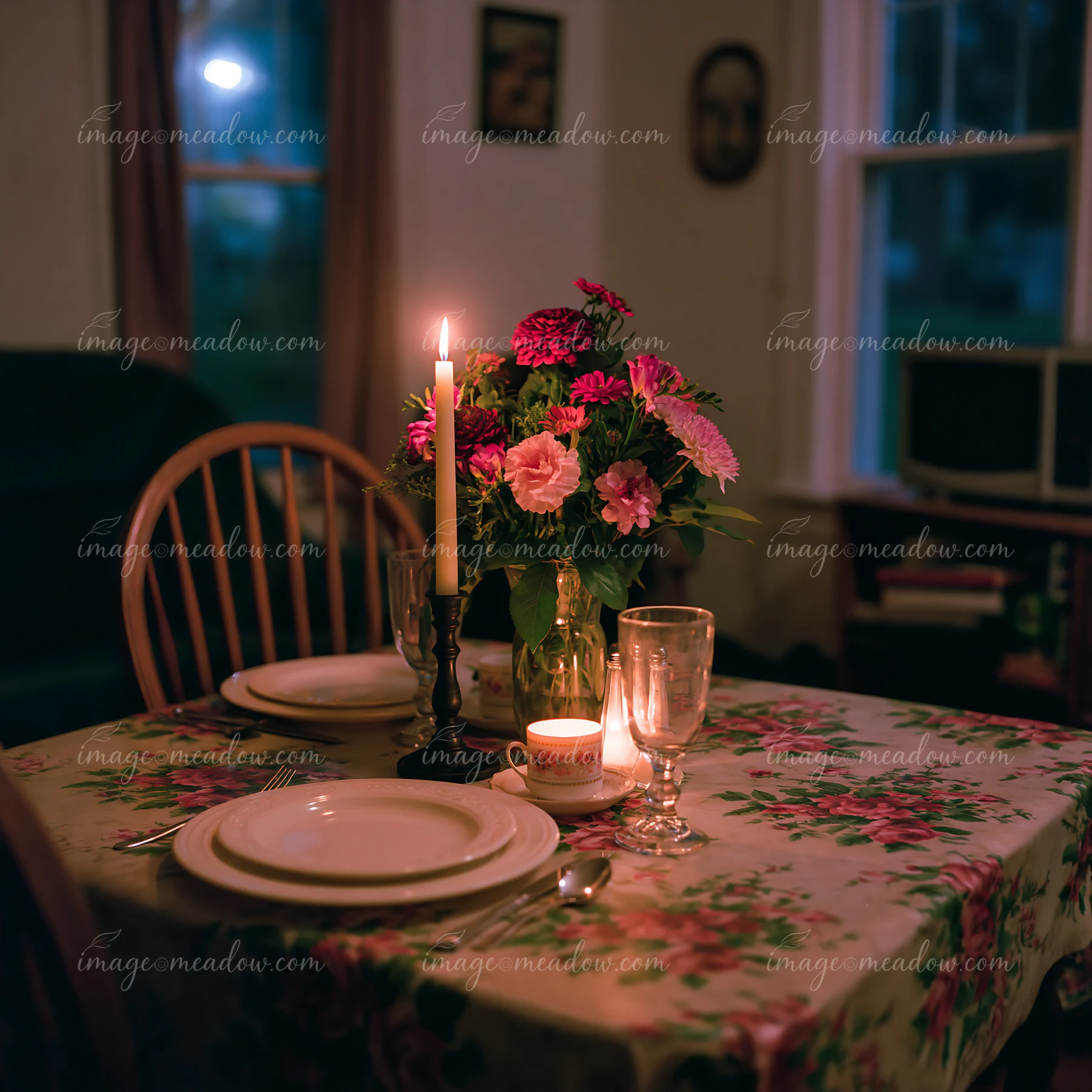 Empty dining chair beside sympathy flowers and a candlelit dining table in a dim home interior.