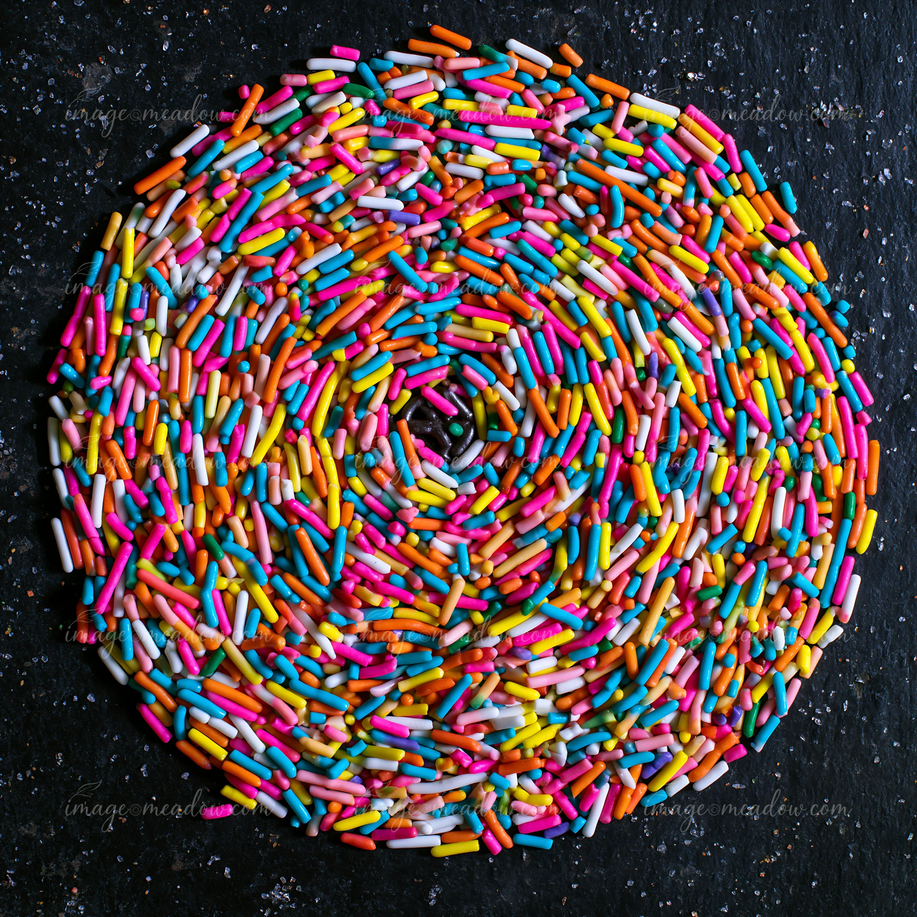 Rainbow sprinkles arranged in a swirl create a colorful design on a dark surface.