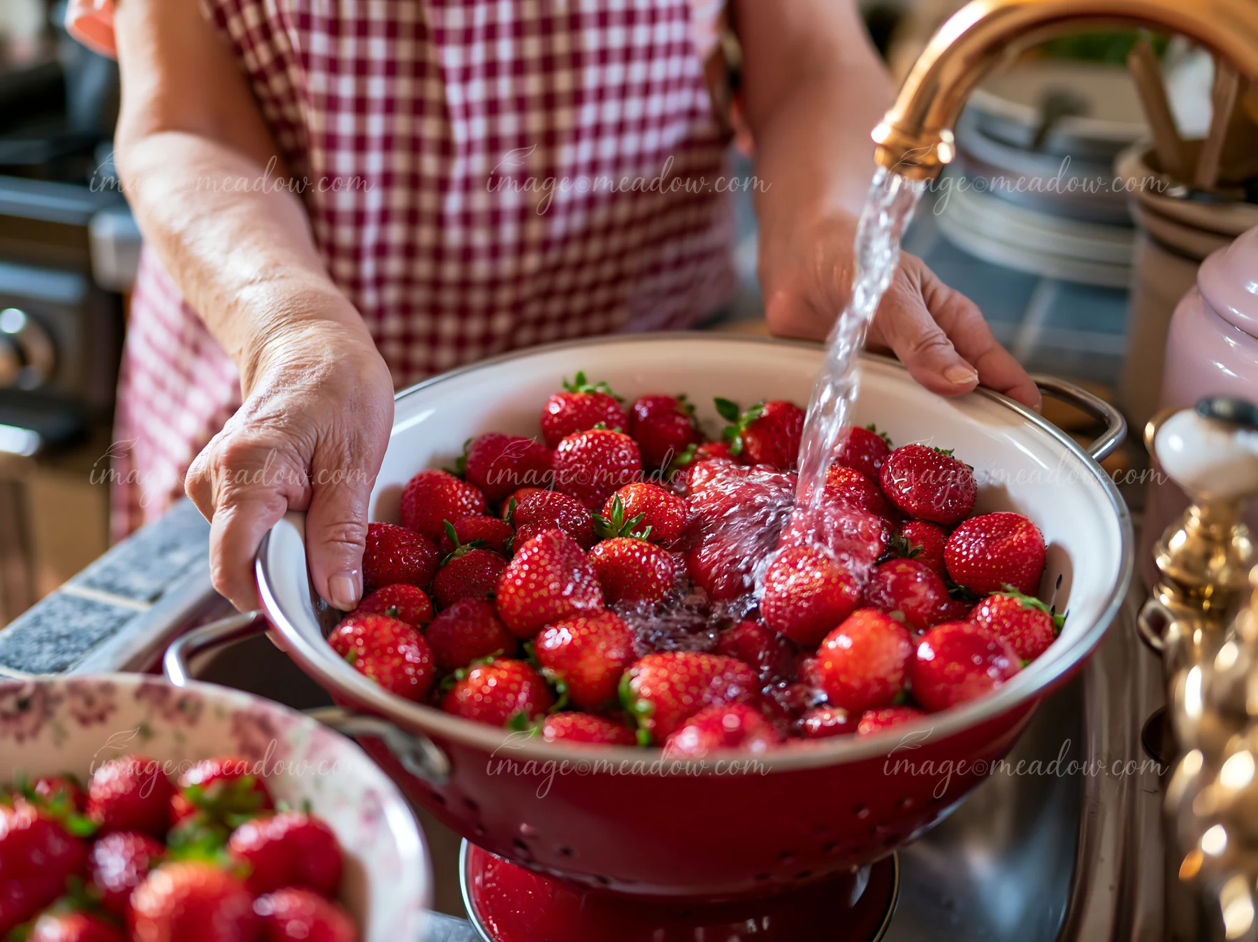 Senior woman with dementia preparing simple food washes strawberries in a bowl at a kitchen sink.
