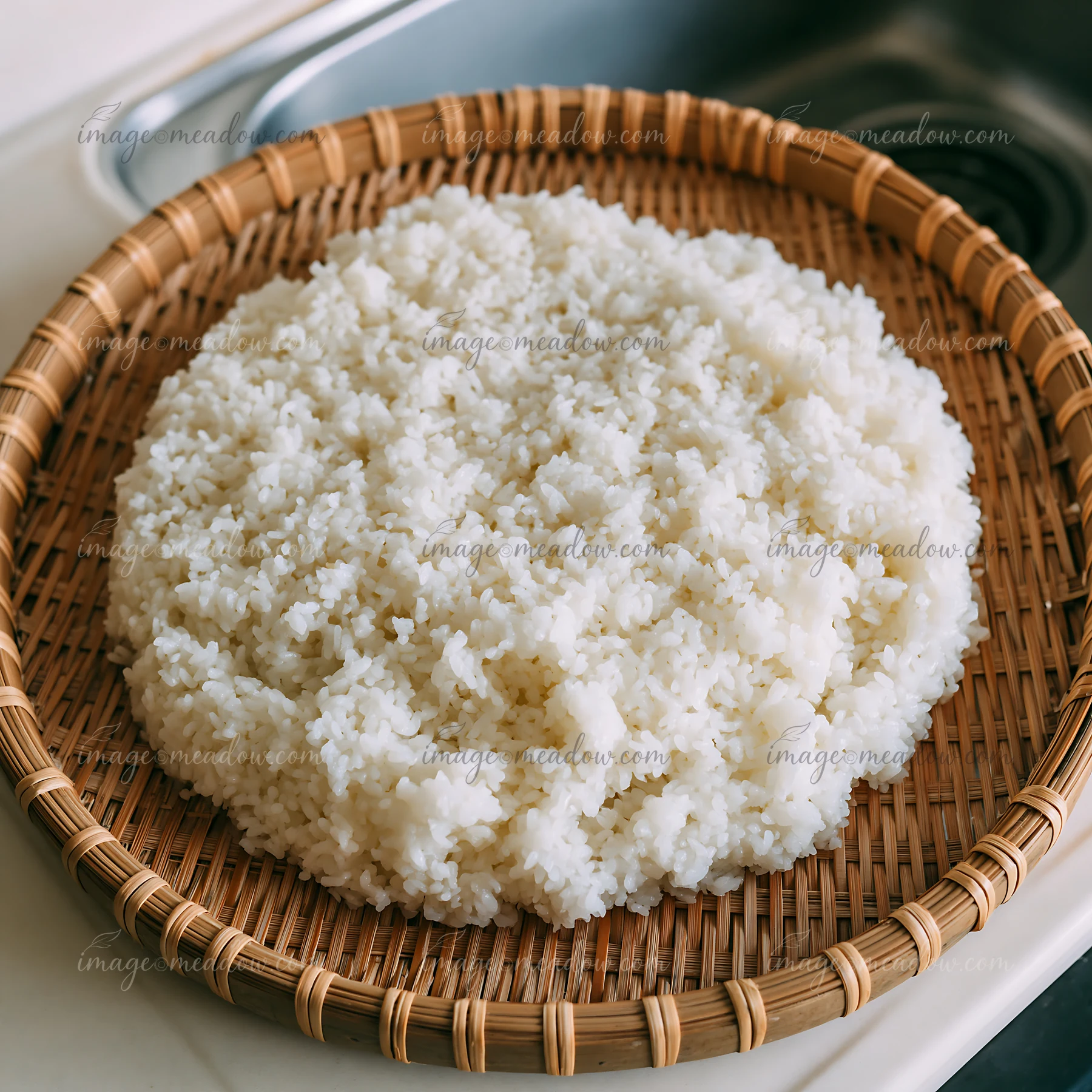 Sushi rice cooling on tray is shown in a woven basket placed on a kitchen counter.
