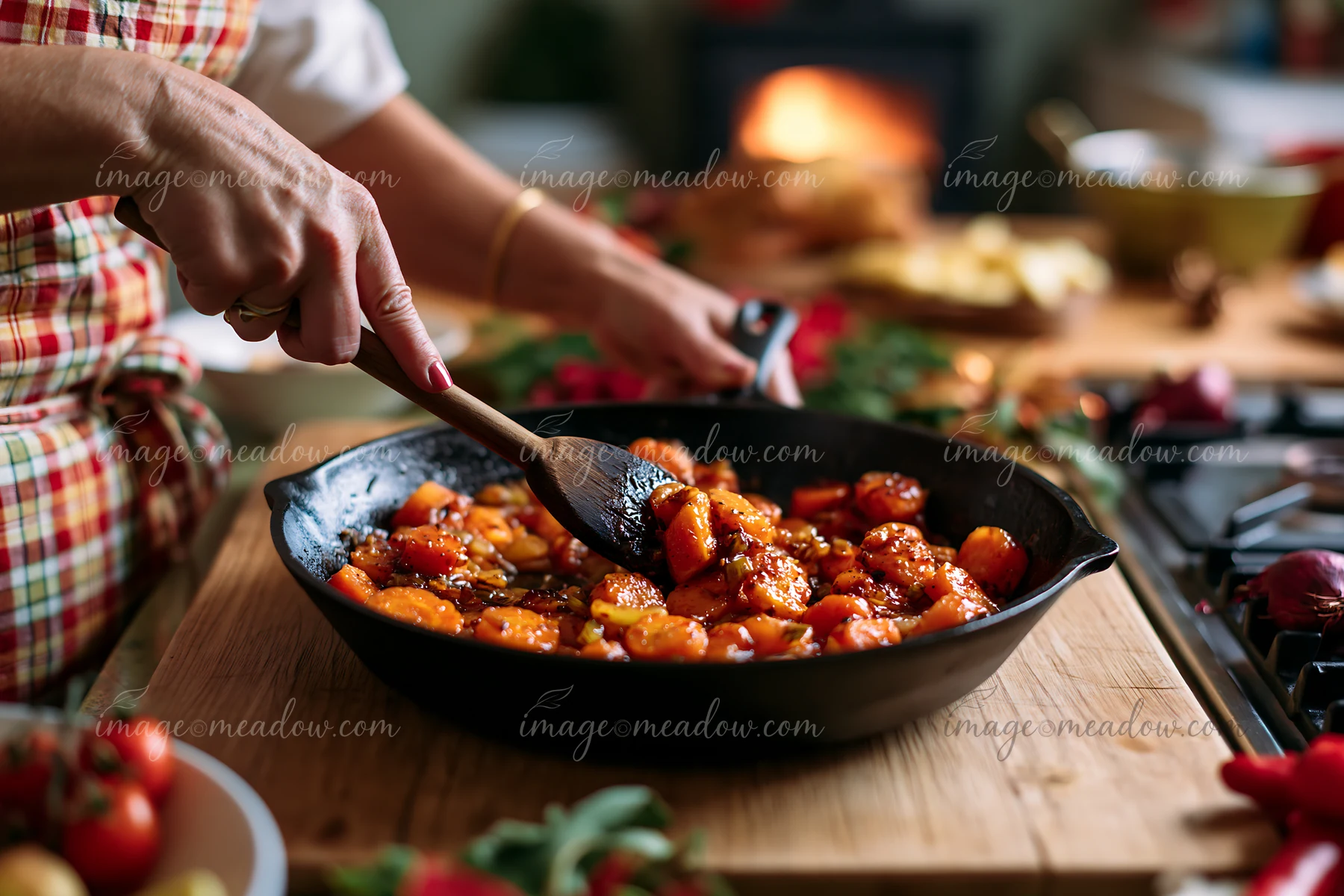 Sweet potatoes are being cooked in a skillet as part of Christmas dinner preparation in a warm kitchen with a fireplace.