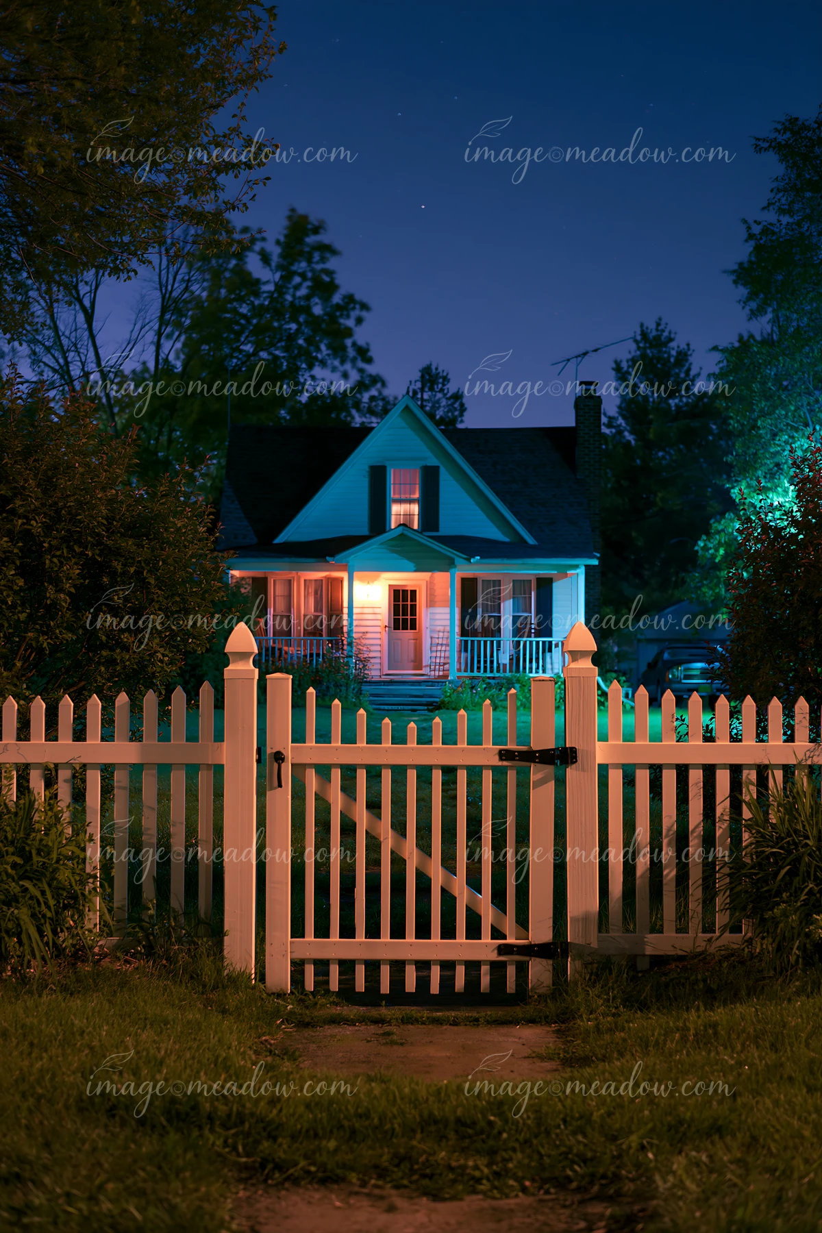 The image features a country home with a white fence illuminated at night under a clear sky.