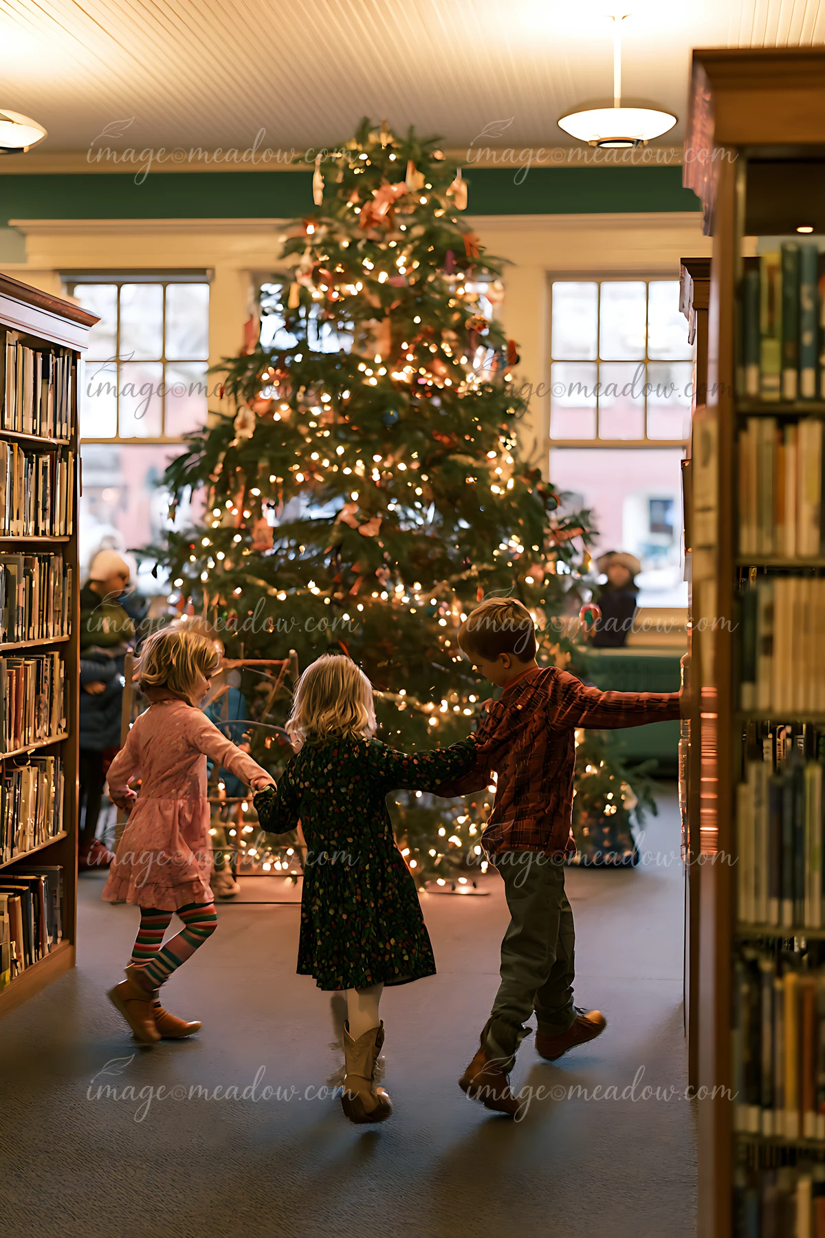 Three children dance around a decorated Christmas tree in a warmly lit library.