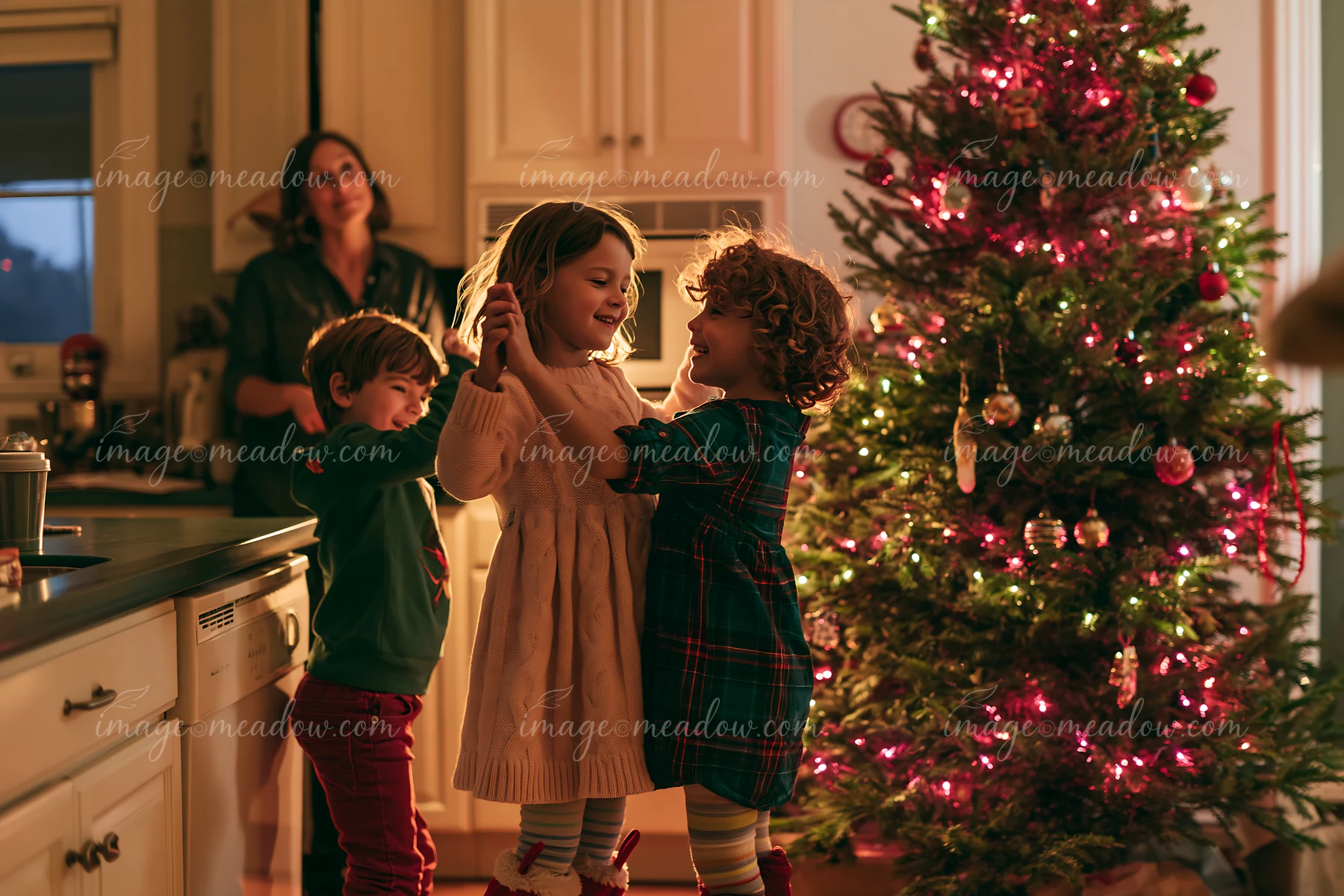 Three children dance beside a decorated Christmas tree in a warmly lit home.