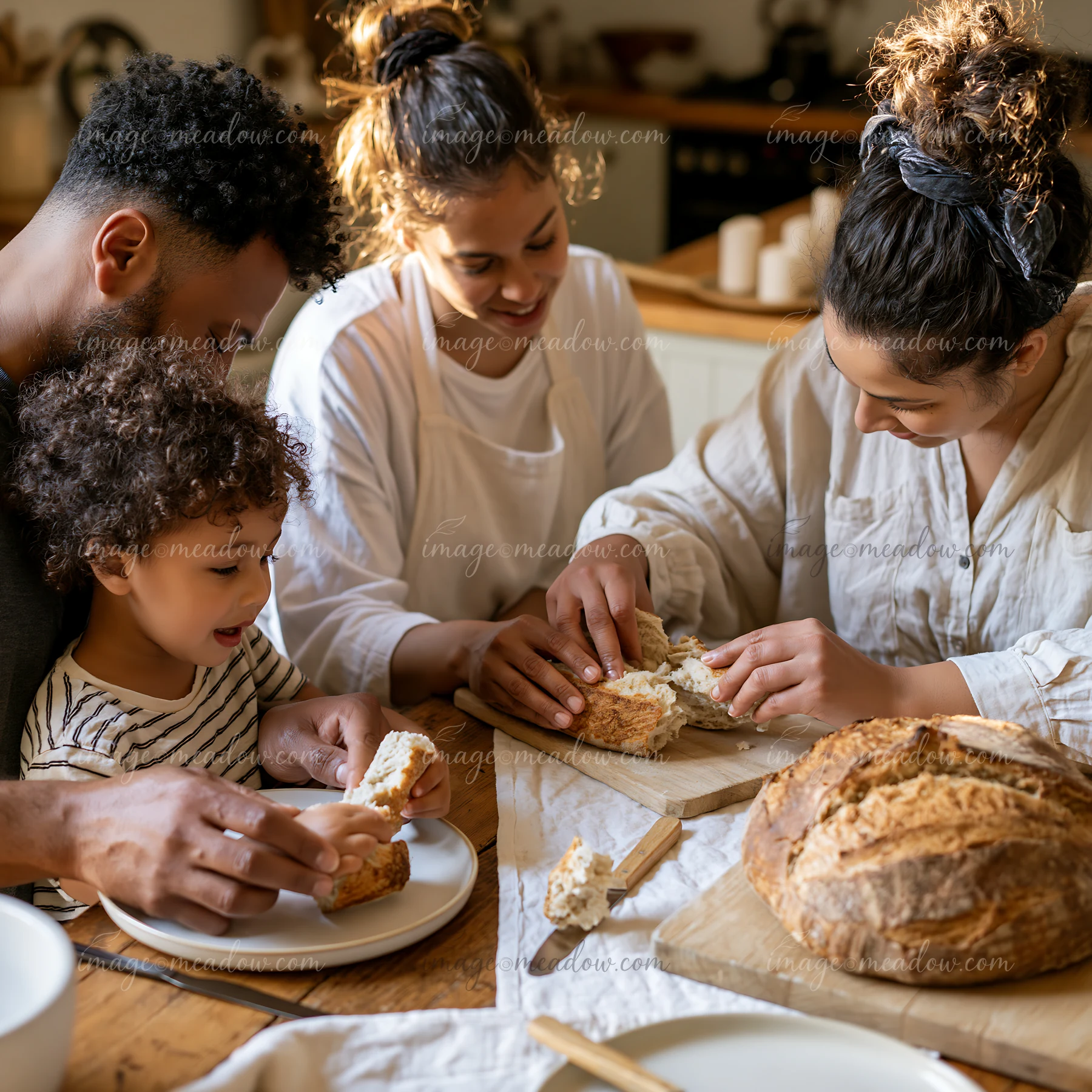Two adults and two children share freshly baked bread around a wooden kitchen table.