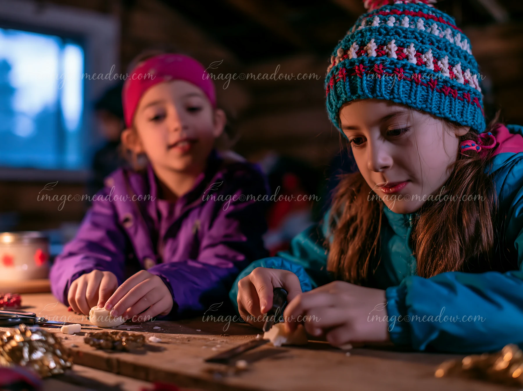Two children sit at a wooden table inside a workshop, focused on making handmade ornaments.