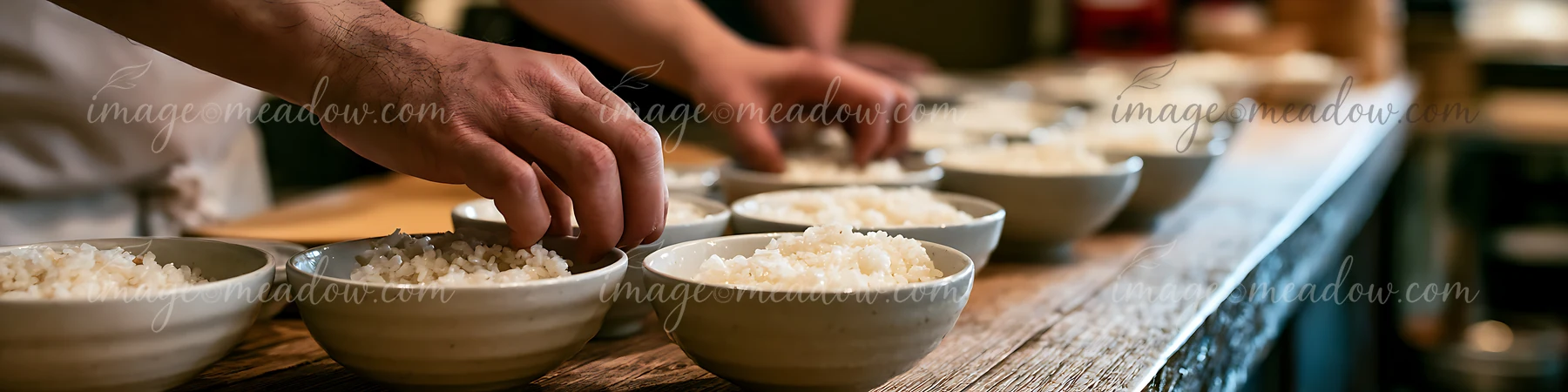 Two sushi chefs place rice into bowls in a busy restaurant kitchen.