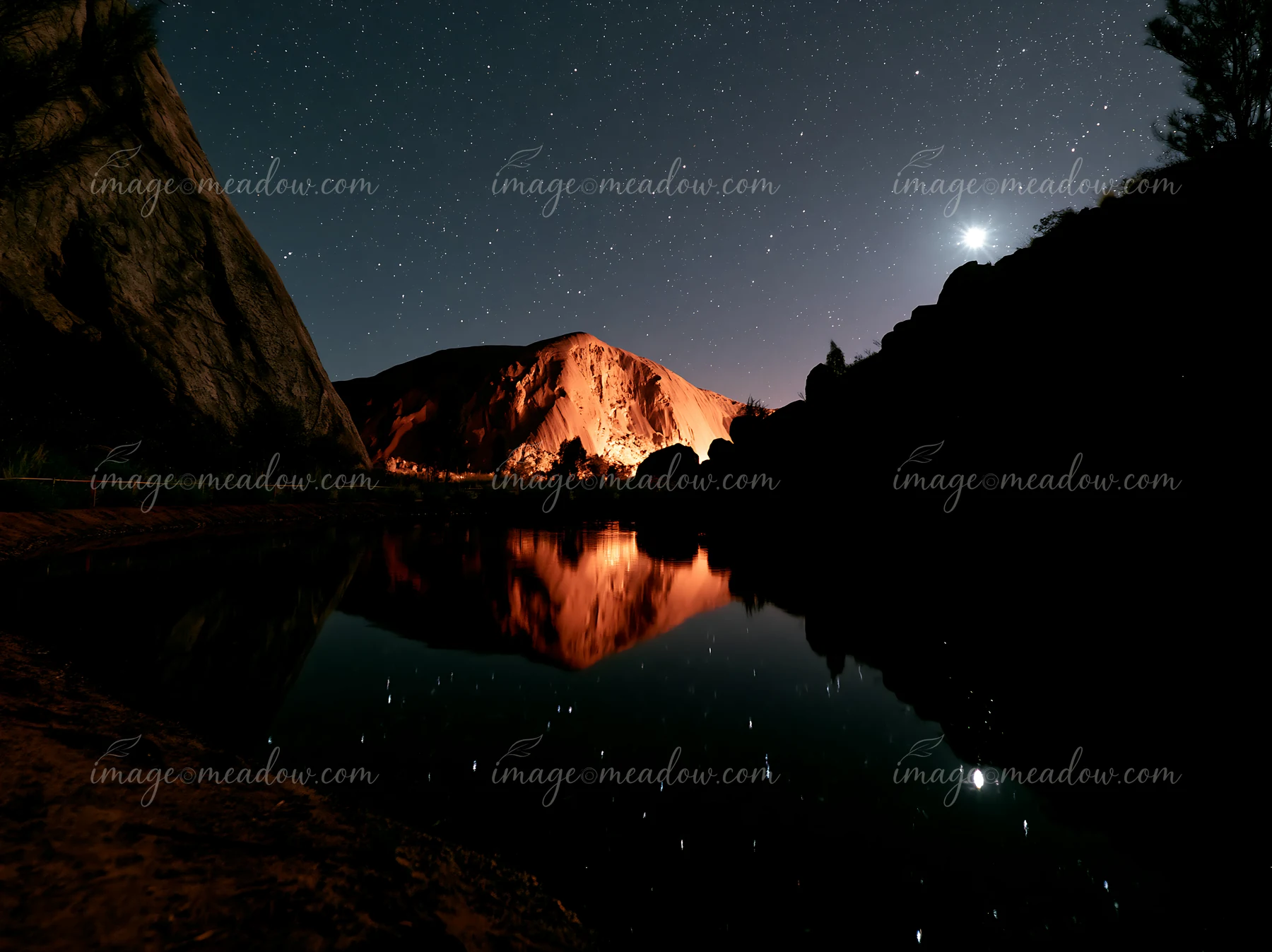 Uluru stands tall under a starry night sky, surrounded by rocky formations.