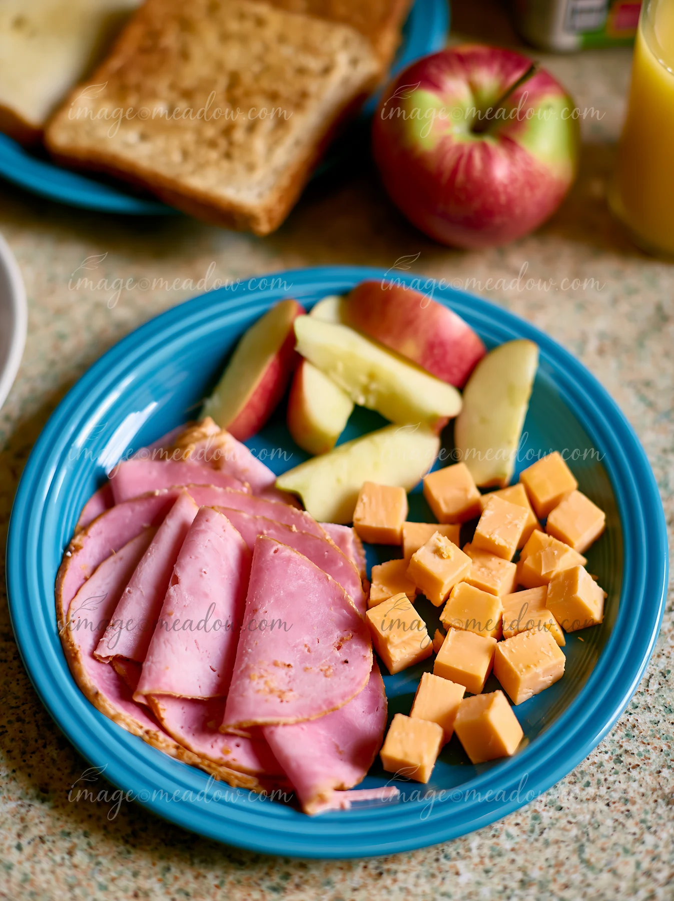 A breakfast plate with cold cuts, cheese, and fresh apple slices is set on a kitchen counter.