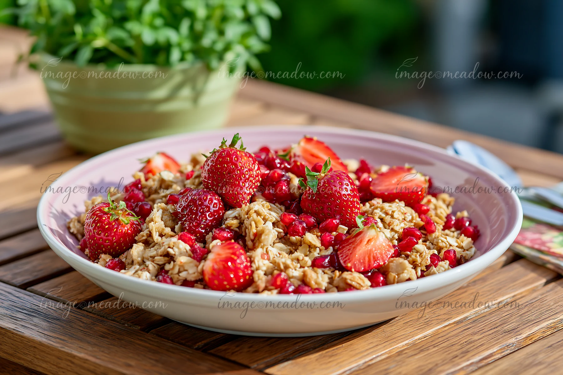 A breakfast plate with muesli features strawberries and pomegranate on a wooden table.