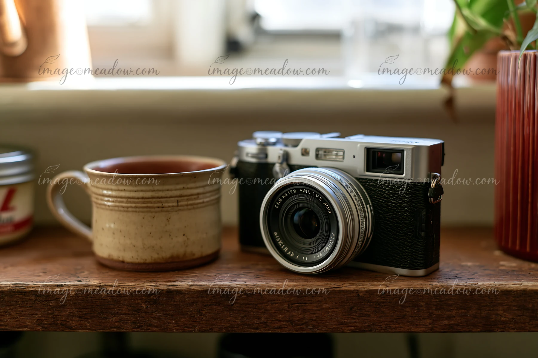 A camera and lens on a wooden shelf sit next to a ceramic cup.
