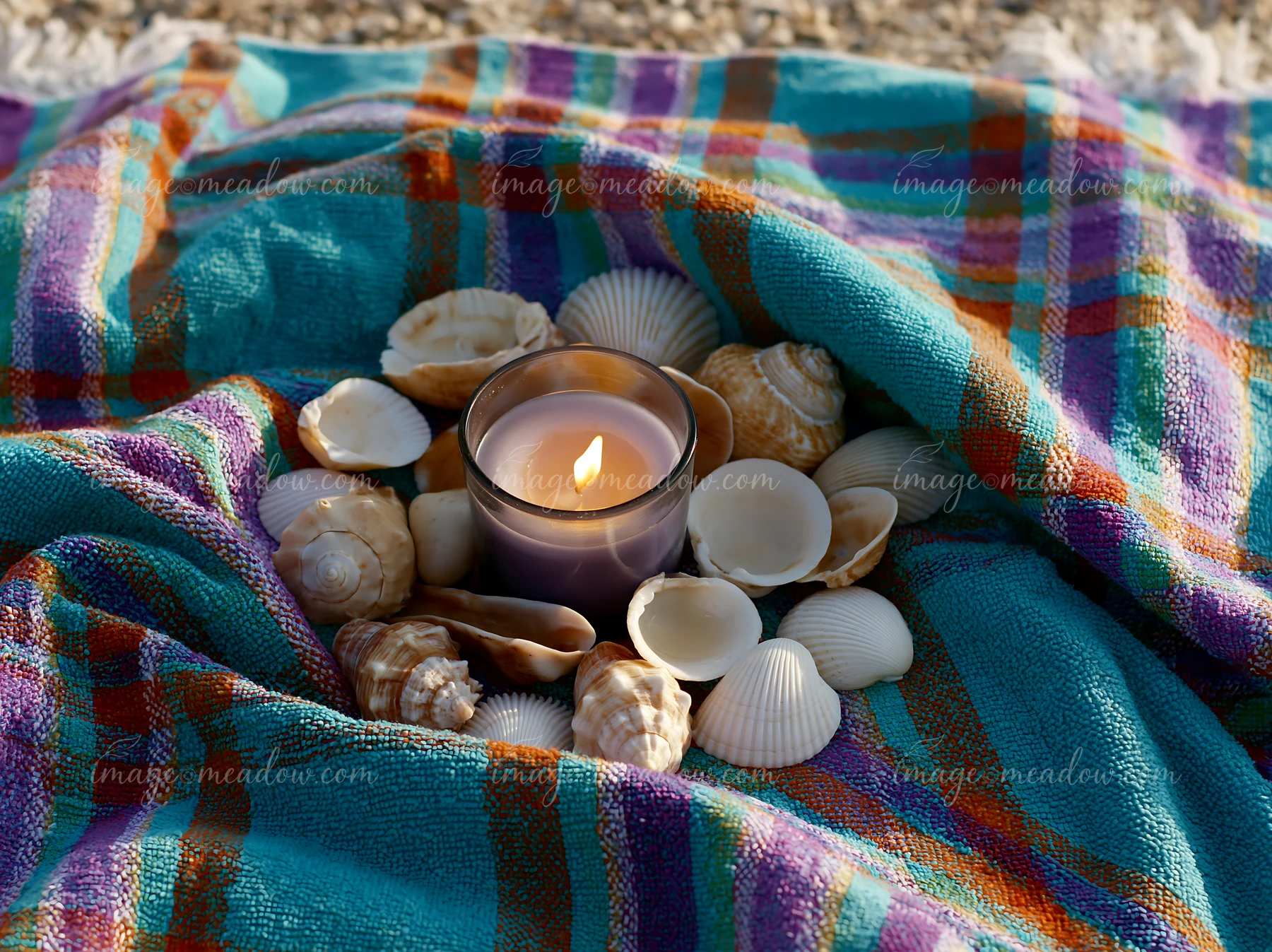 A candle surrounded by seashells sits on a colorful fabric, capturing a moment at the beach.